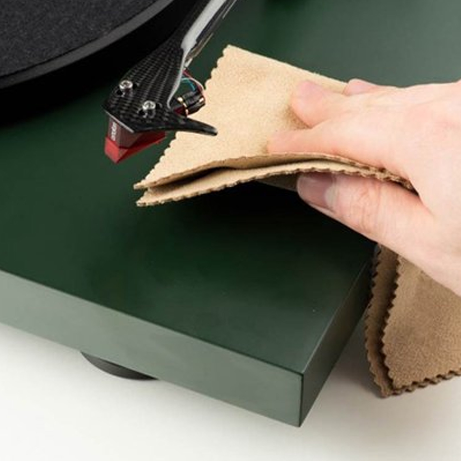 Ręka wyciera gramofon ściereczką. Odtwarzacz jest ciemnozielony.