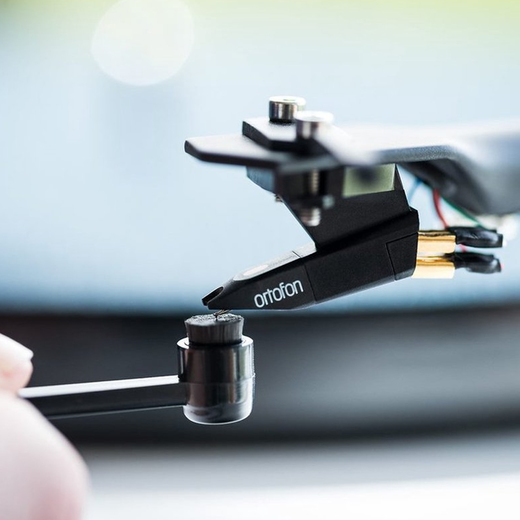 Zbliżenie wkładki gramofonowej z igłą dotykającą płyty, na rozmytym tle.