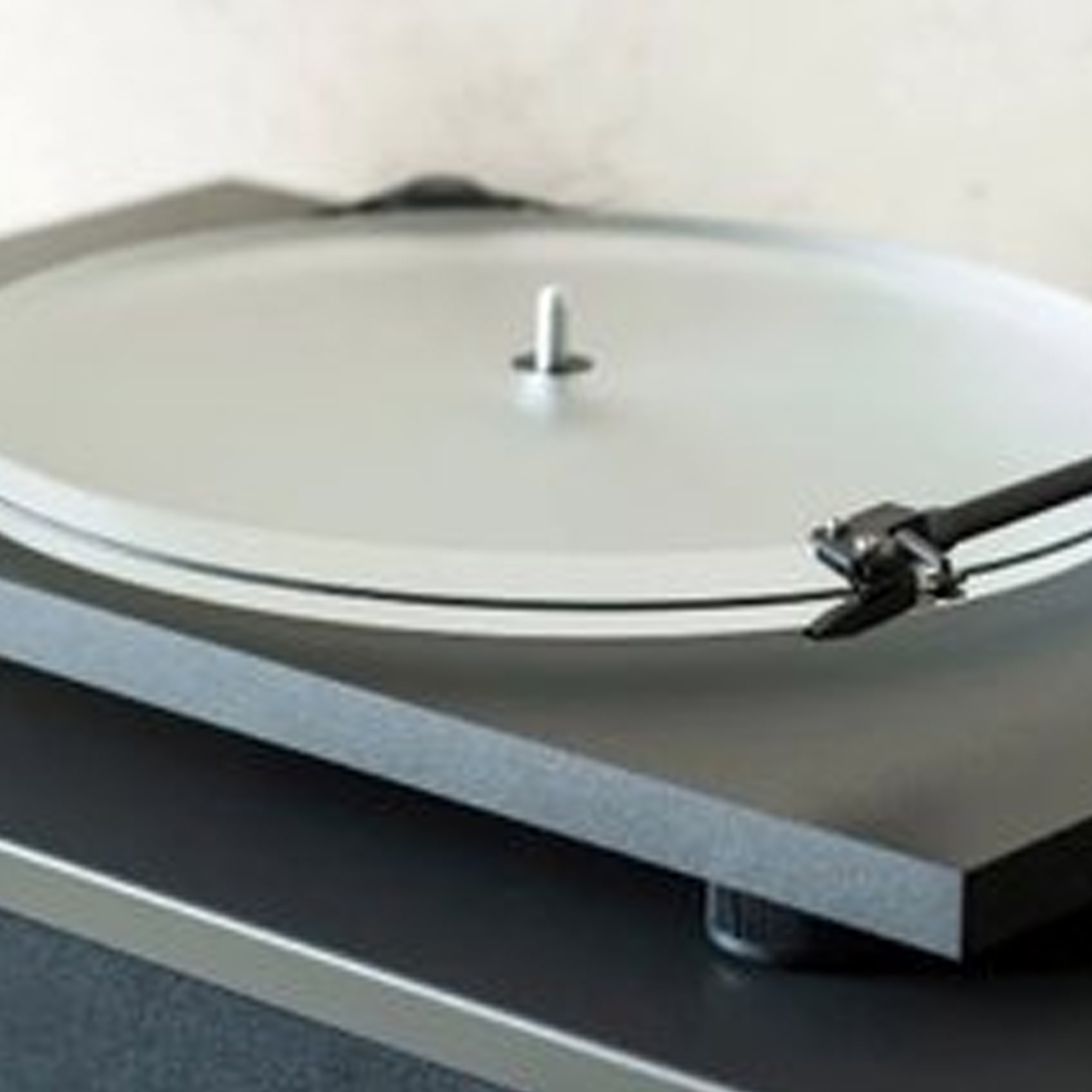 Gramofon z przezroczystym talerzem i ramieniem na czarnej, prostokątnej podstawie.