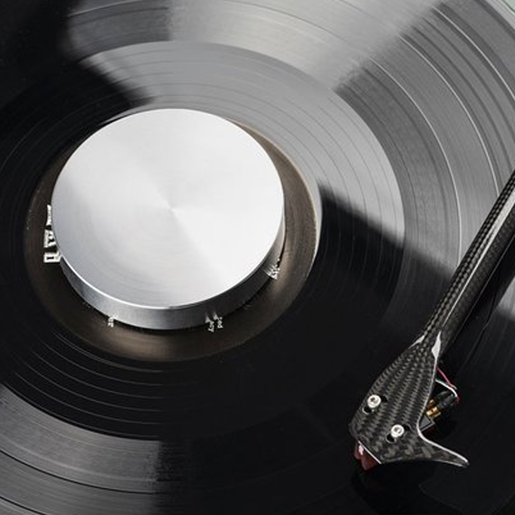 Czarna płyta winylowa ze srebrnym środkiem. Igła jest w rowku. Czarne tło.