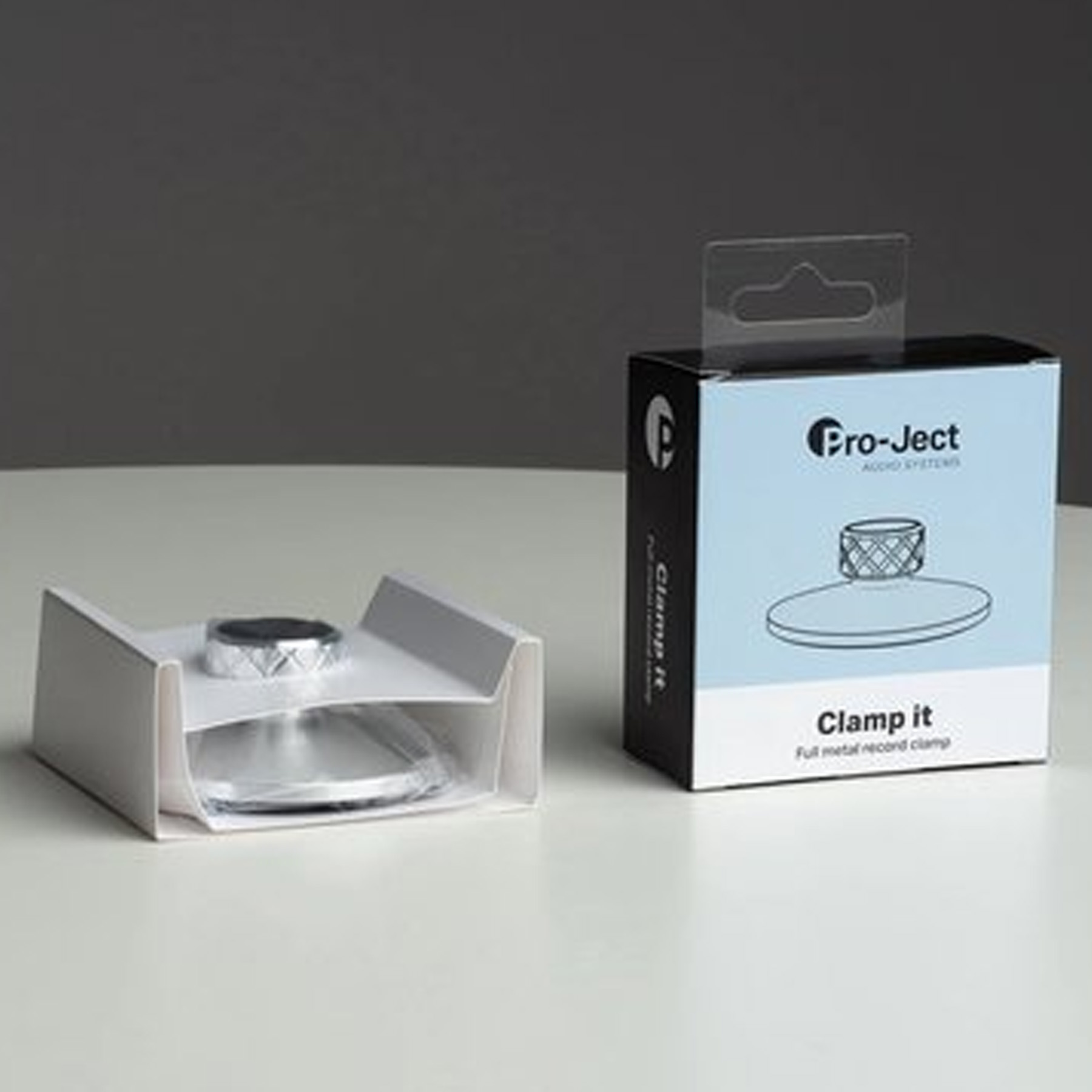 A vinyl record clamp in a box. The clamp is silver with a black and silver top.