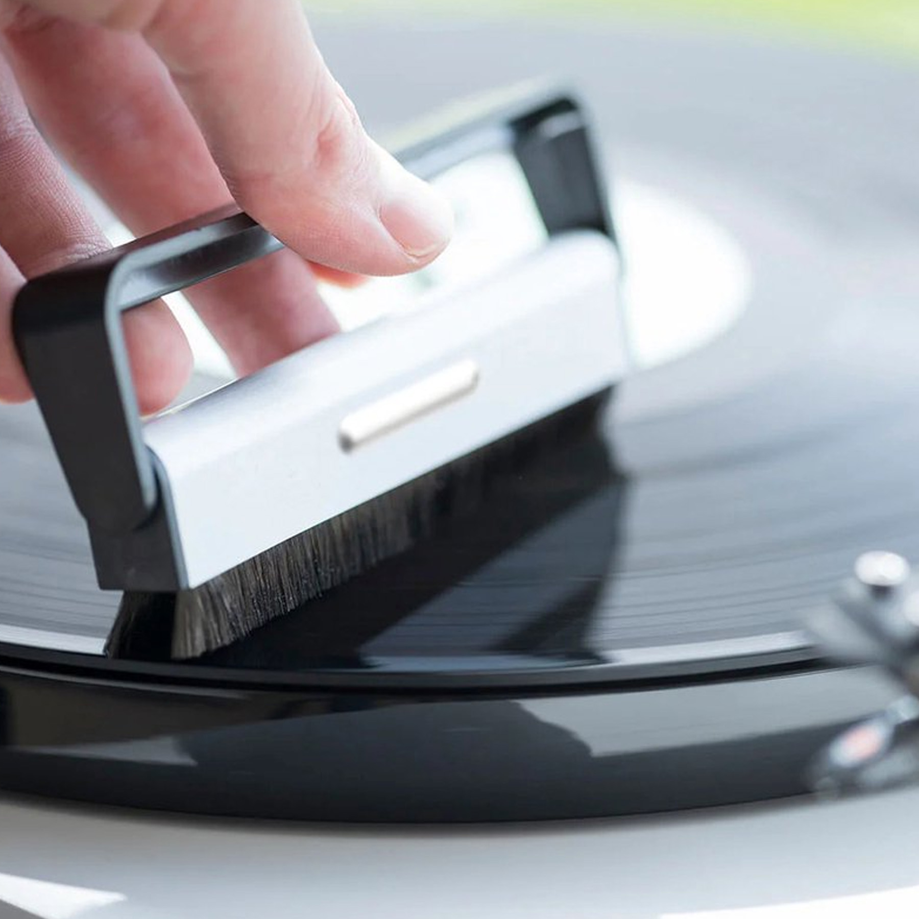 Een hand die een vinylplaat schoonmaakt. De tool heeft een borstel en maakt de plaat schoon.