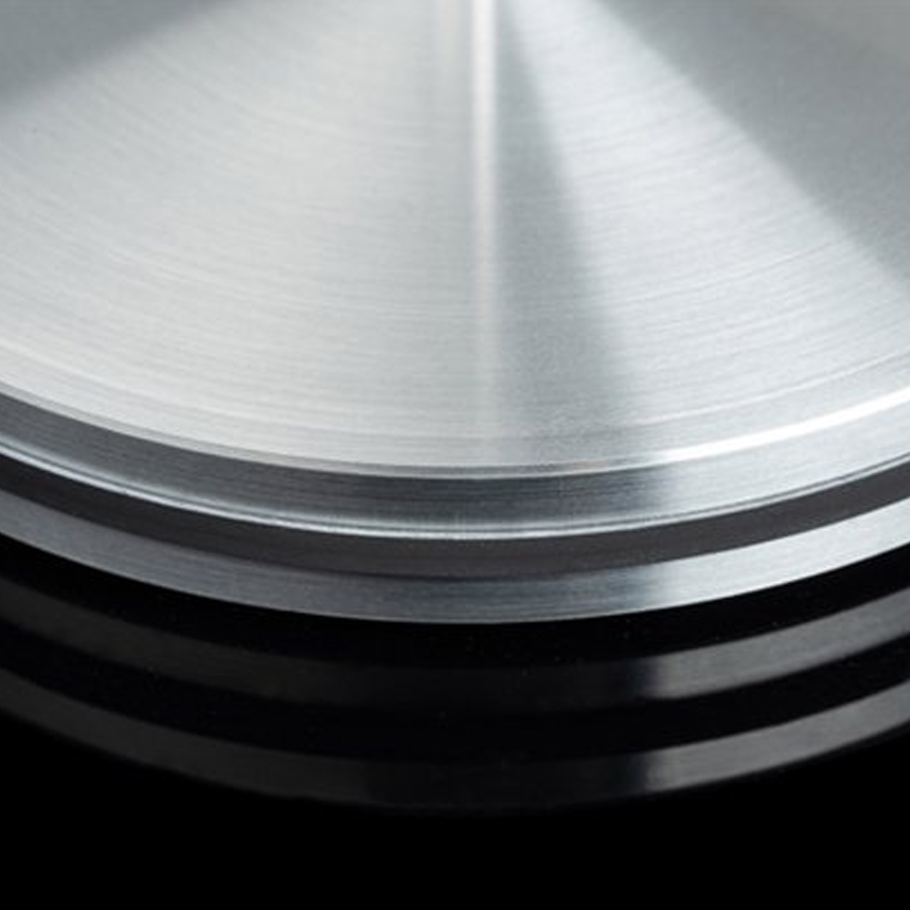 Zbliżenie błyszczącej, metalowej powierzchni z koncentrycznymi, okrągłymi rowkami. Czarne tło.