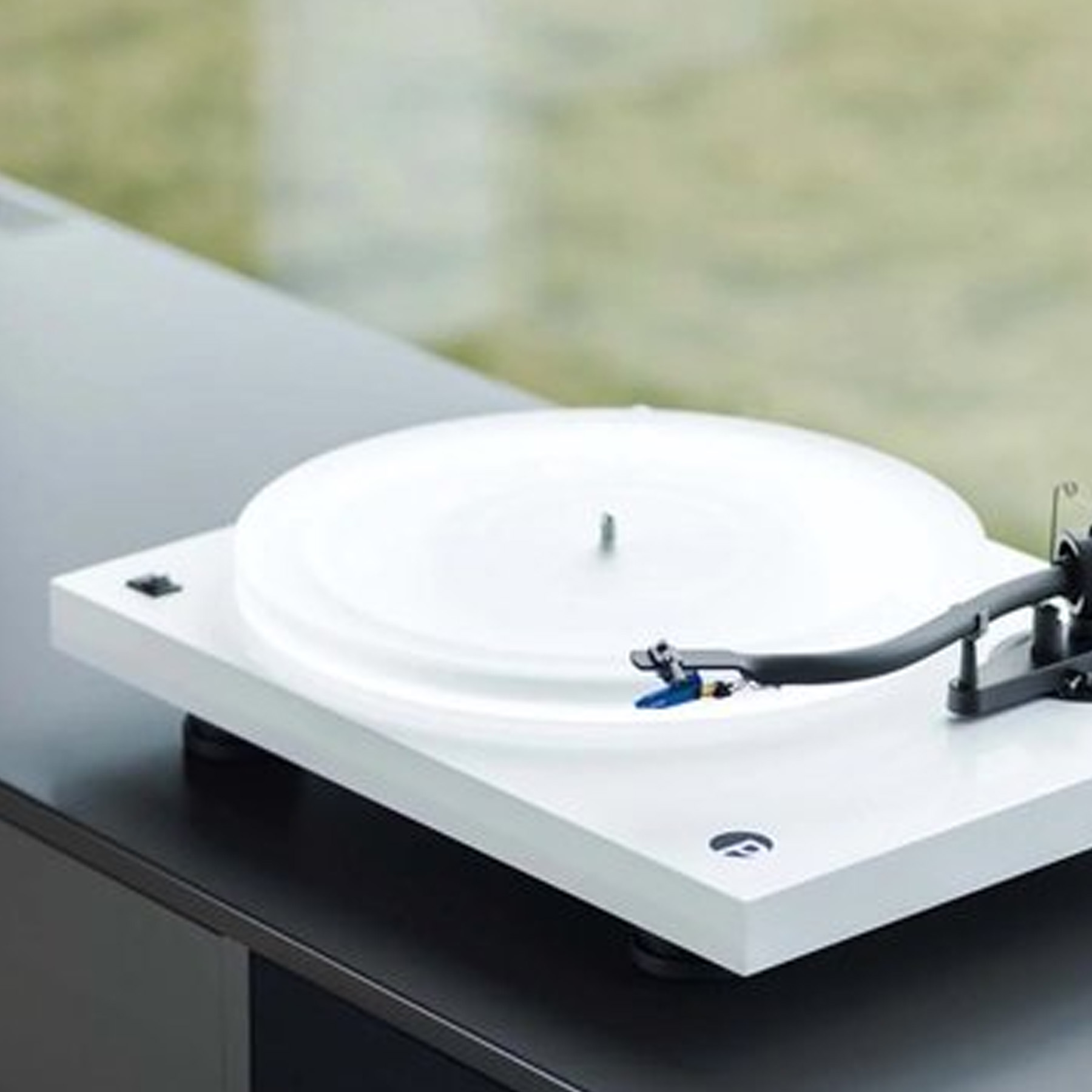 Biały gramofon stoi na czarnej powierzchni, widoczny jest winyl i ramię.