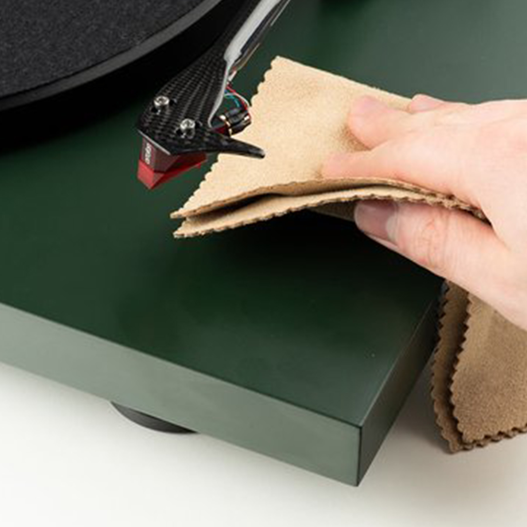 Dłoń czyszcząca gramofon. Gramofon jest ciemnozielony i ma srebrne ramię.