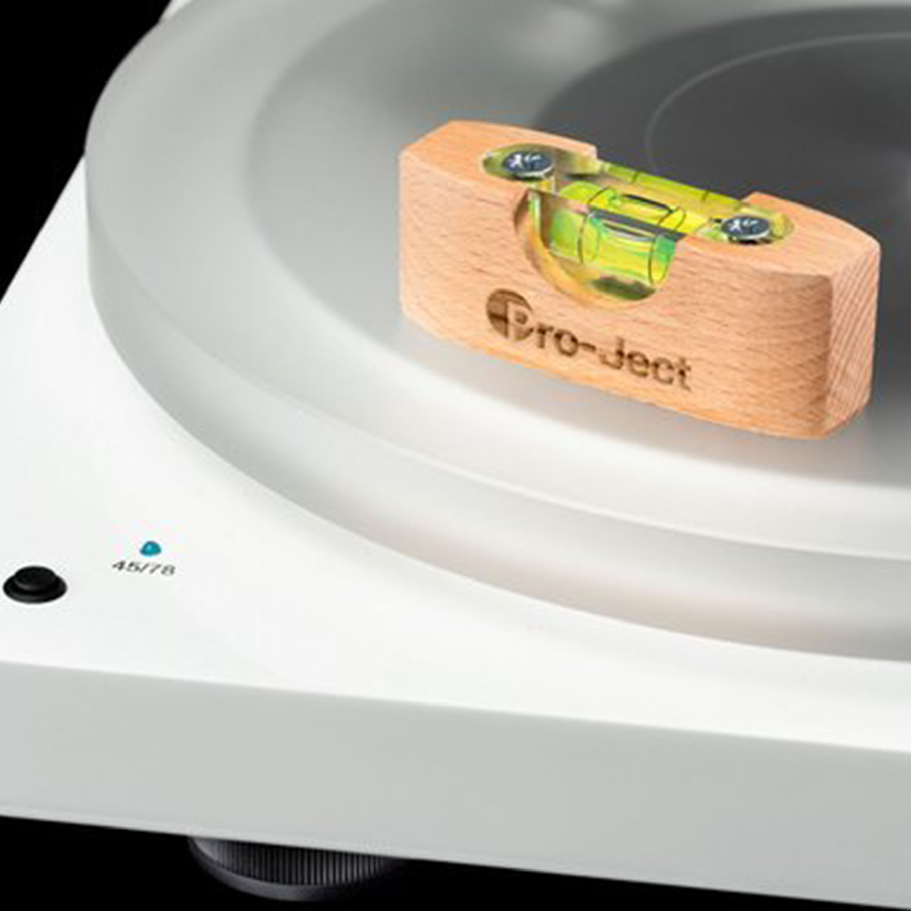 Zbliżenie drewnianego poziomicy z pęcherzykiem w środku, spoczywającego na białym gramofonie. Napis Pro-ject.