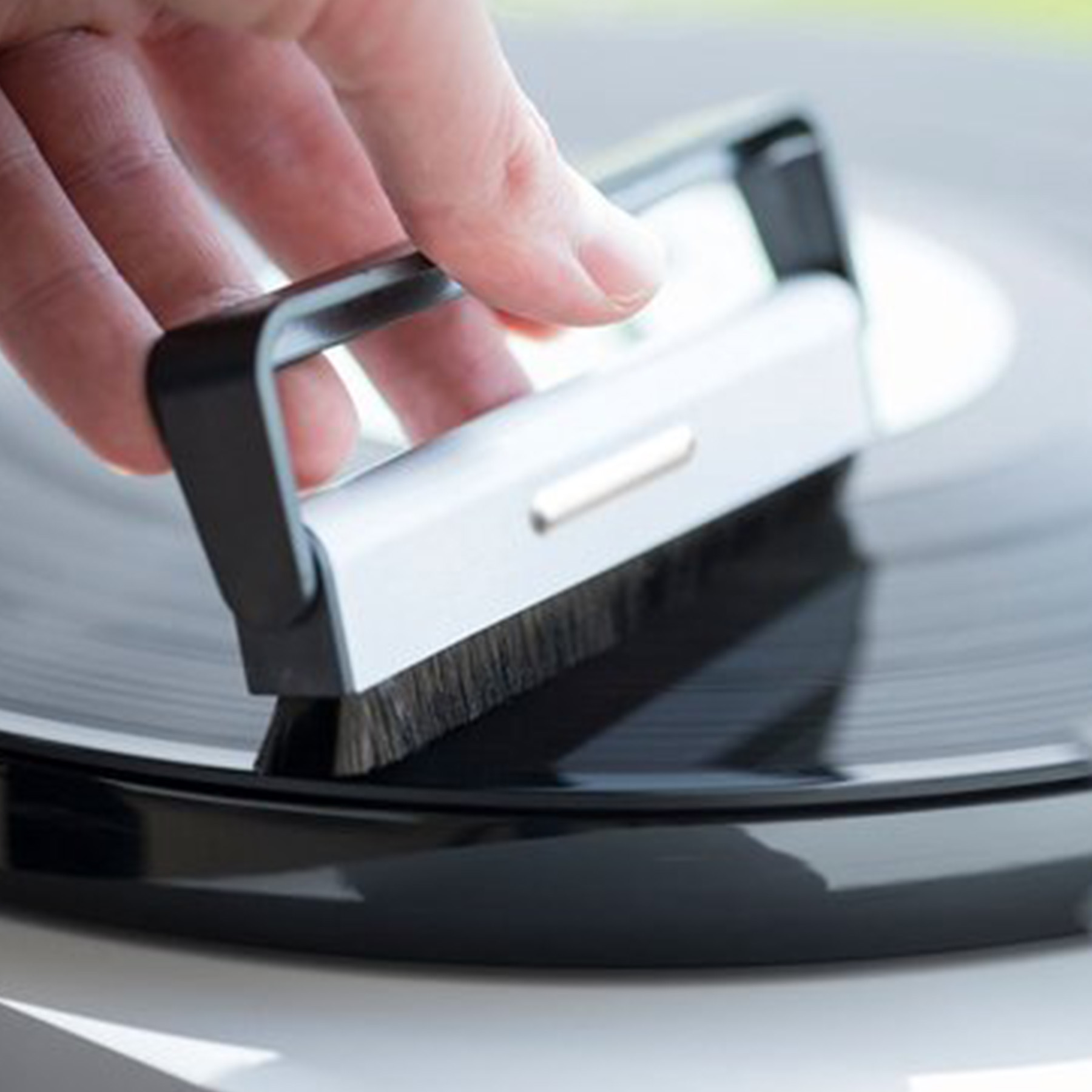 Ręka czyszcząca płytę winylową szczotką. Płyta jest czarna i błyszcząca.