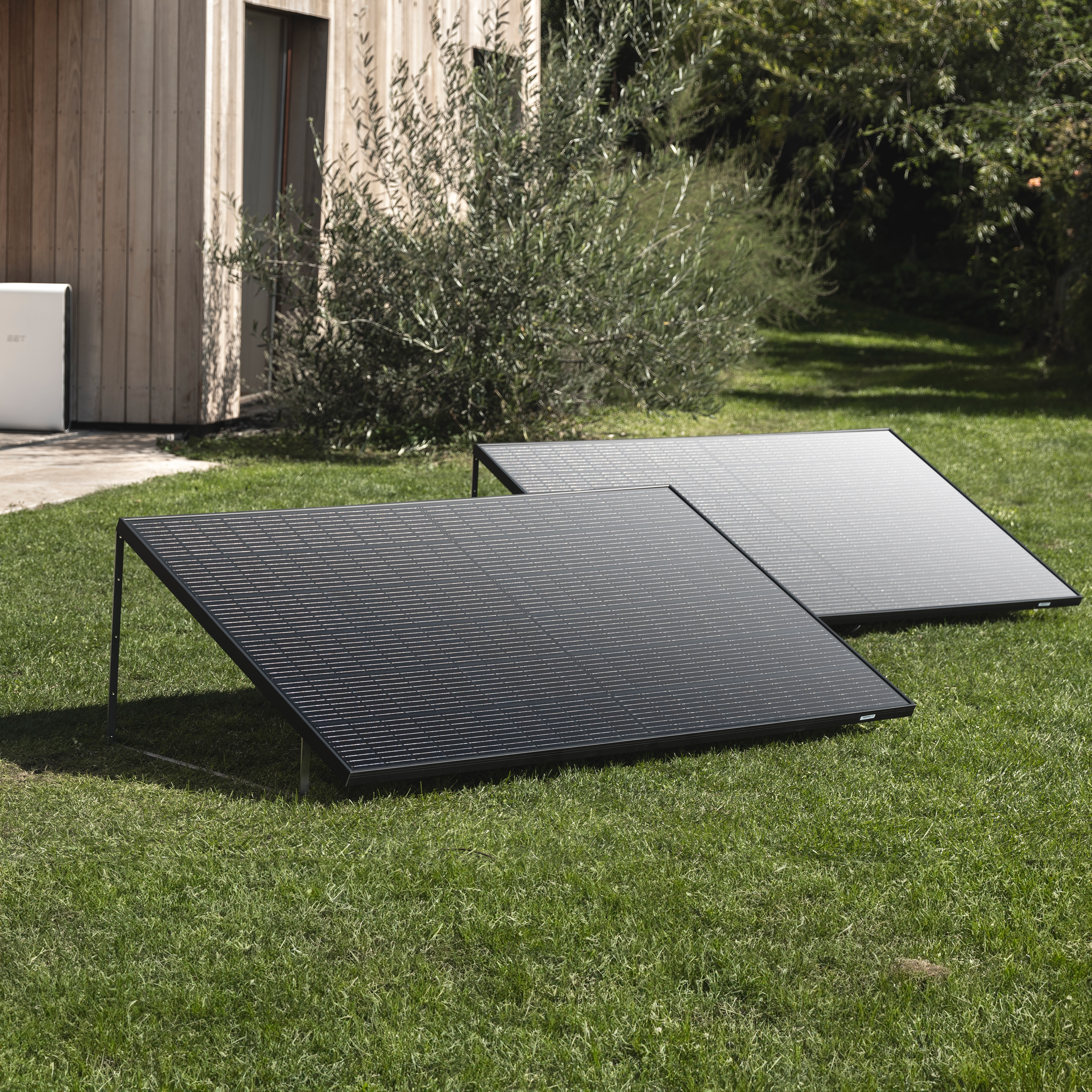 Zwei schwarze Solarmodule auf grünem Gras. Im Hintergrund ein Holzgebäude.