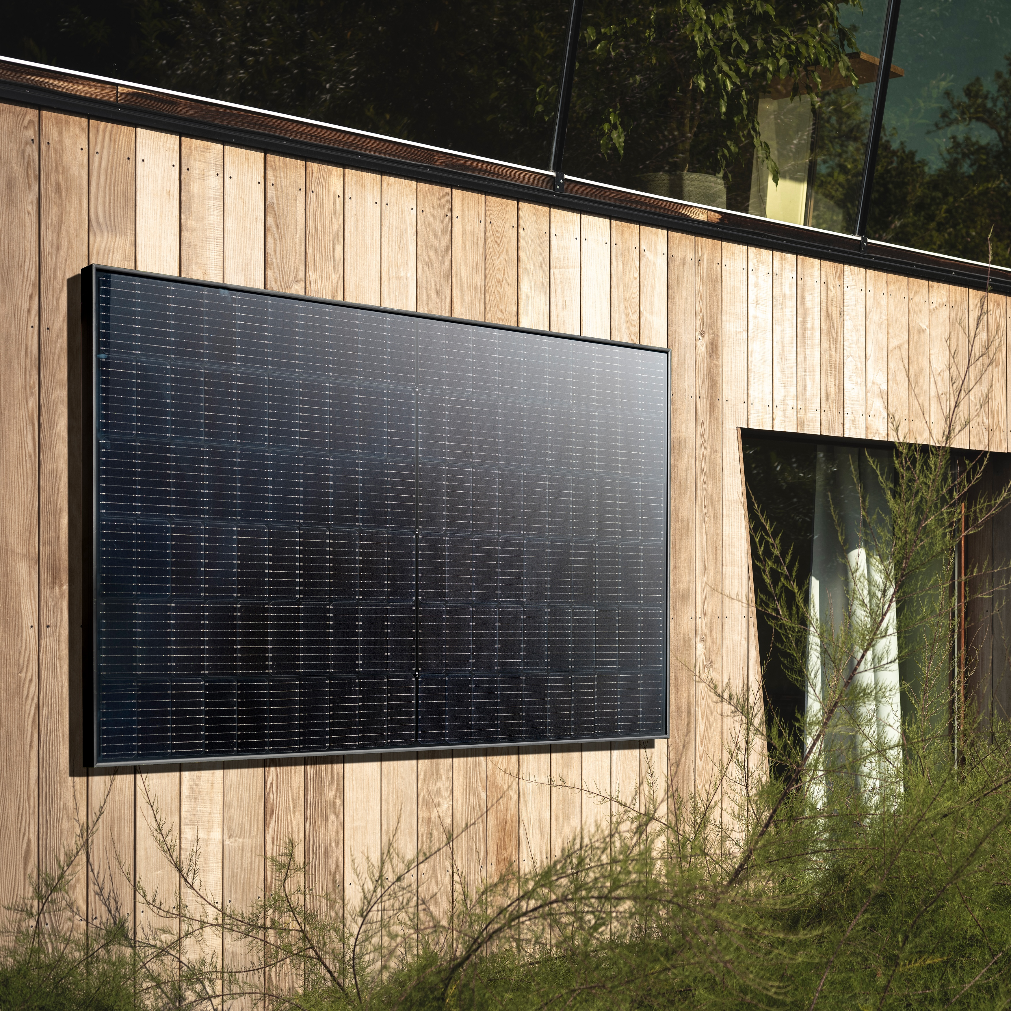 Solarpanel an einem Holzgebäude montiert, mit grüner Vegetation im Vordergrund.