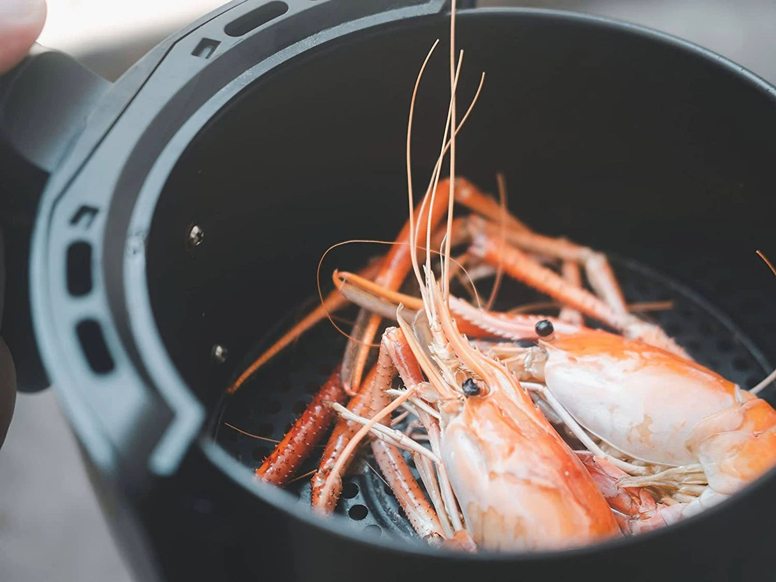 Frytownica powietrzna z ugotowanymi krewetkami w środku. Czarne wnętrze, zbliżenie.