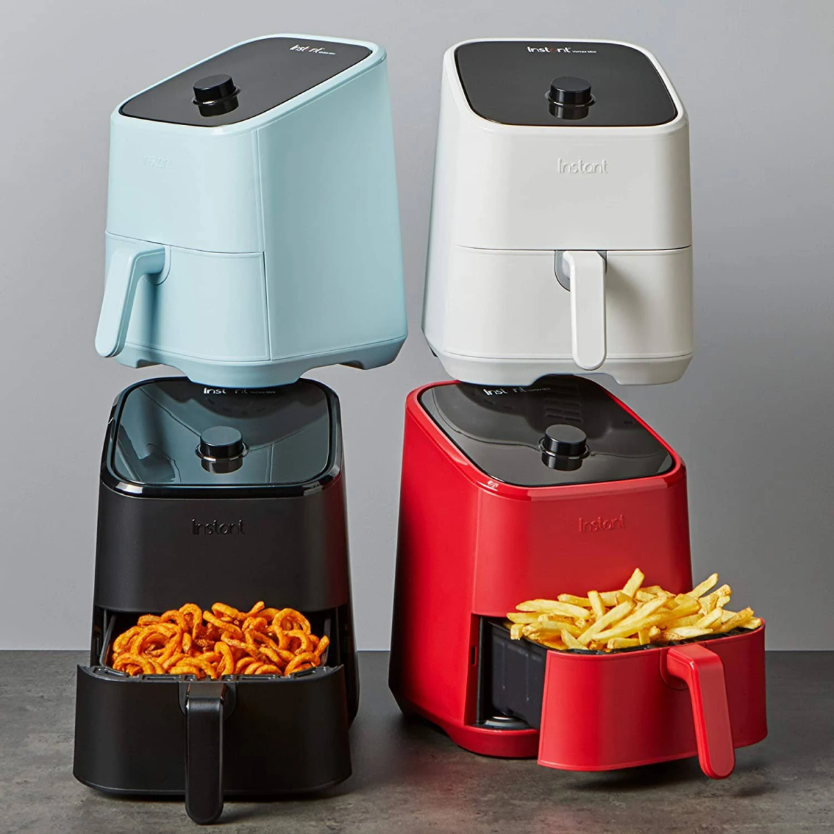 Vier airfryers in verschillende kleuren met eten in de manden.