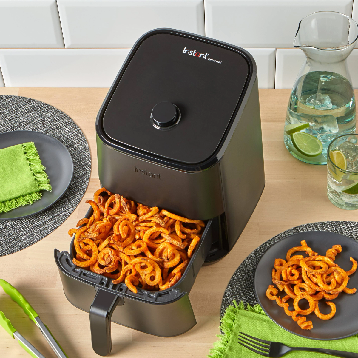 Een airfryer met friet op een bord en in de fryer. De setting is op een houten tafel.