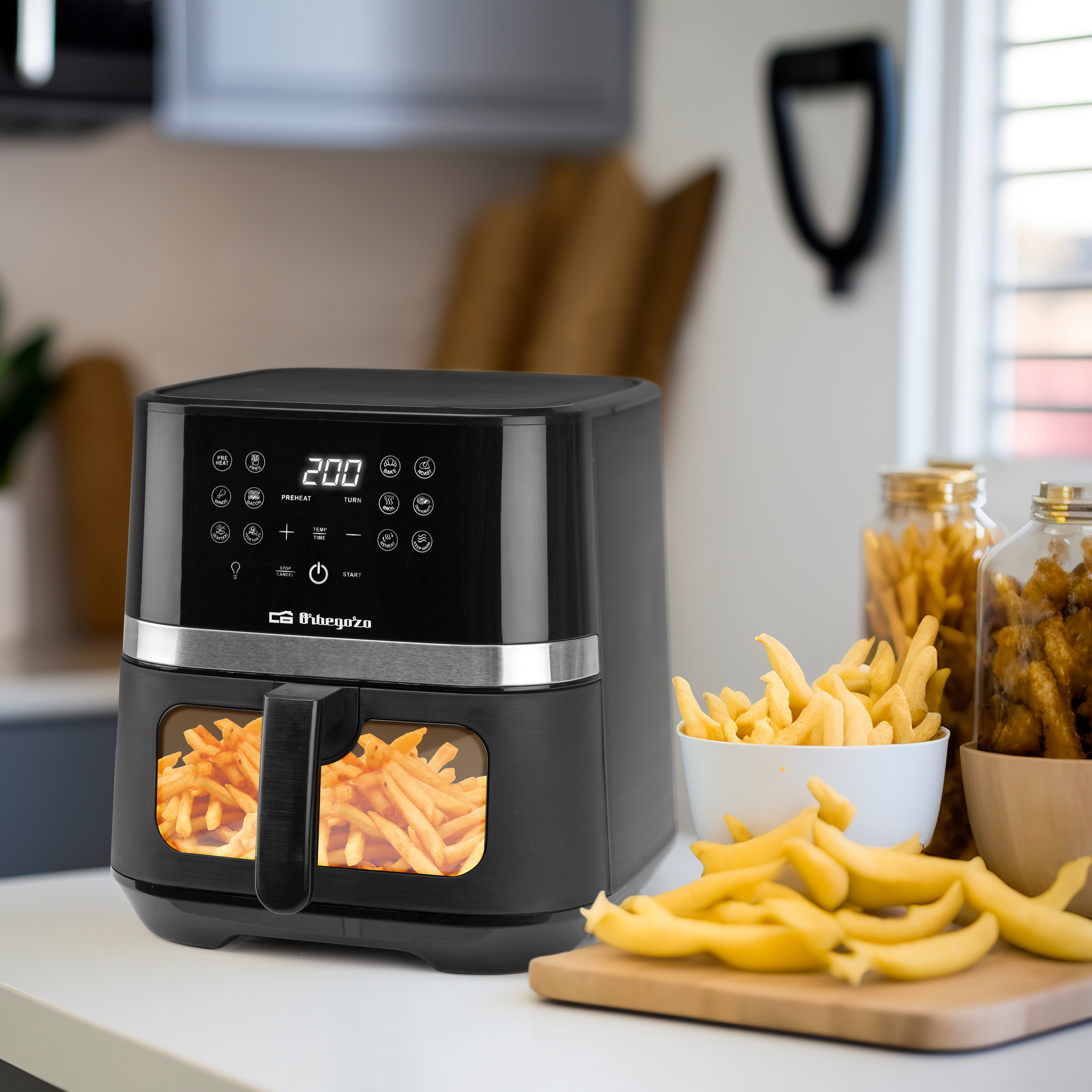 Friggitrice ad aria nera con patatine fritte, una ciotola bianca e un tagliere in legno.