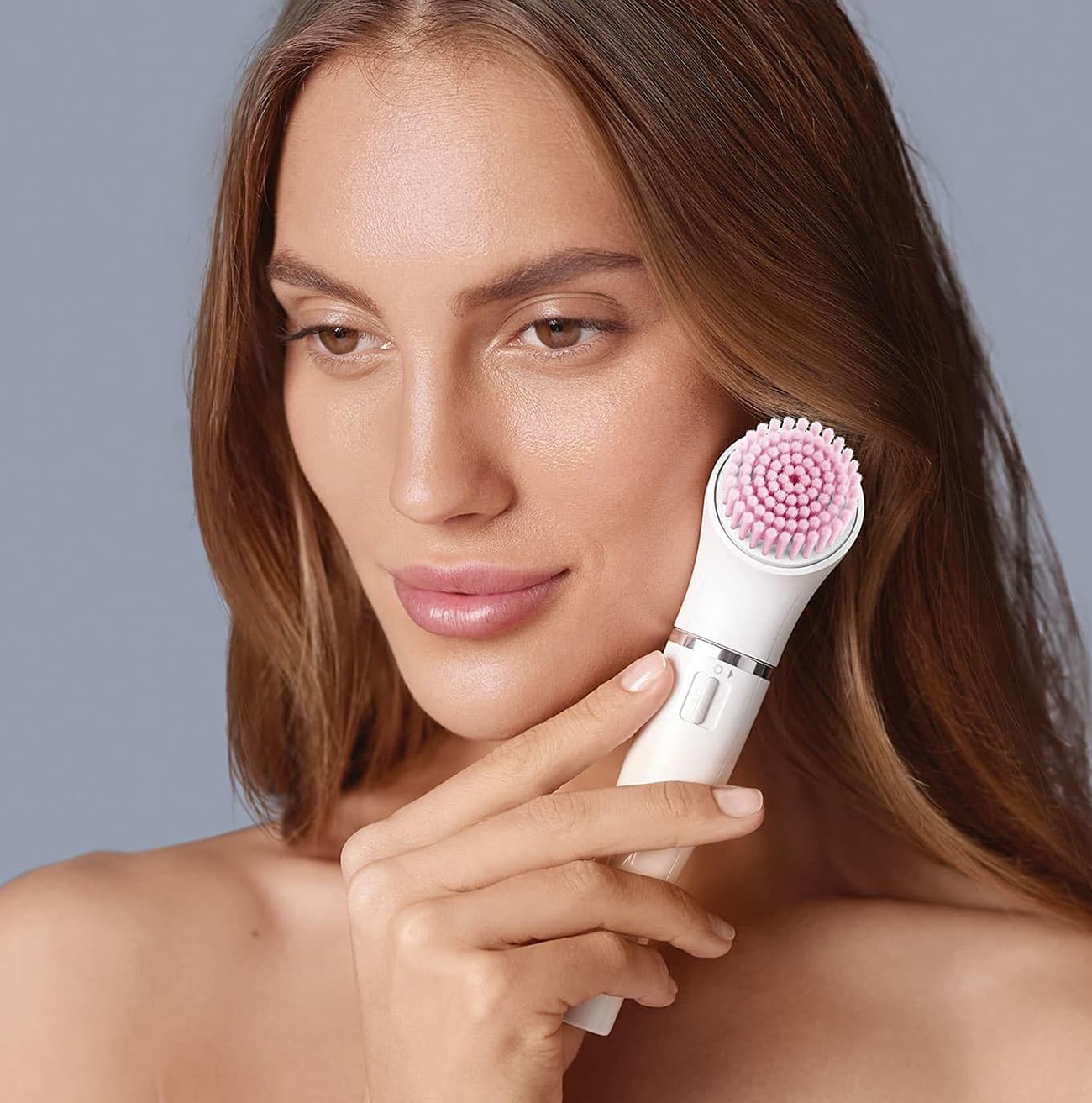 Kobieta używająca szczoteczki do oczyszczania twarzy. Szare tło.