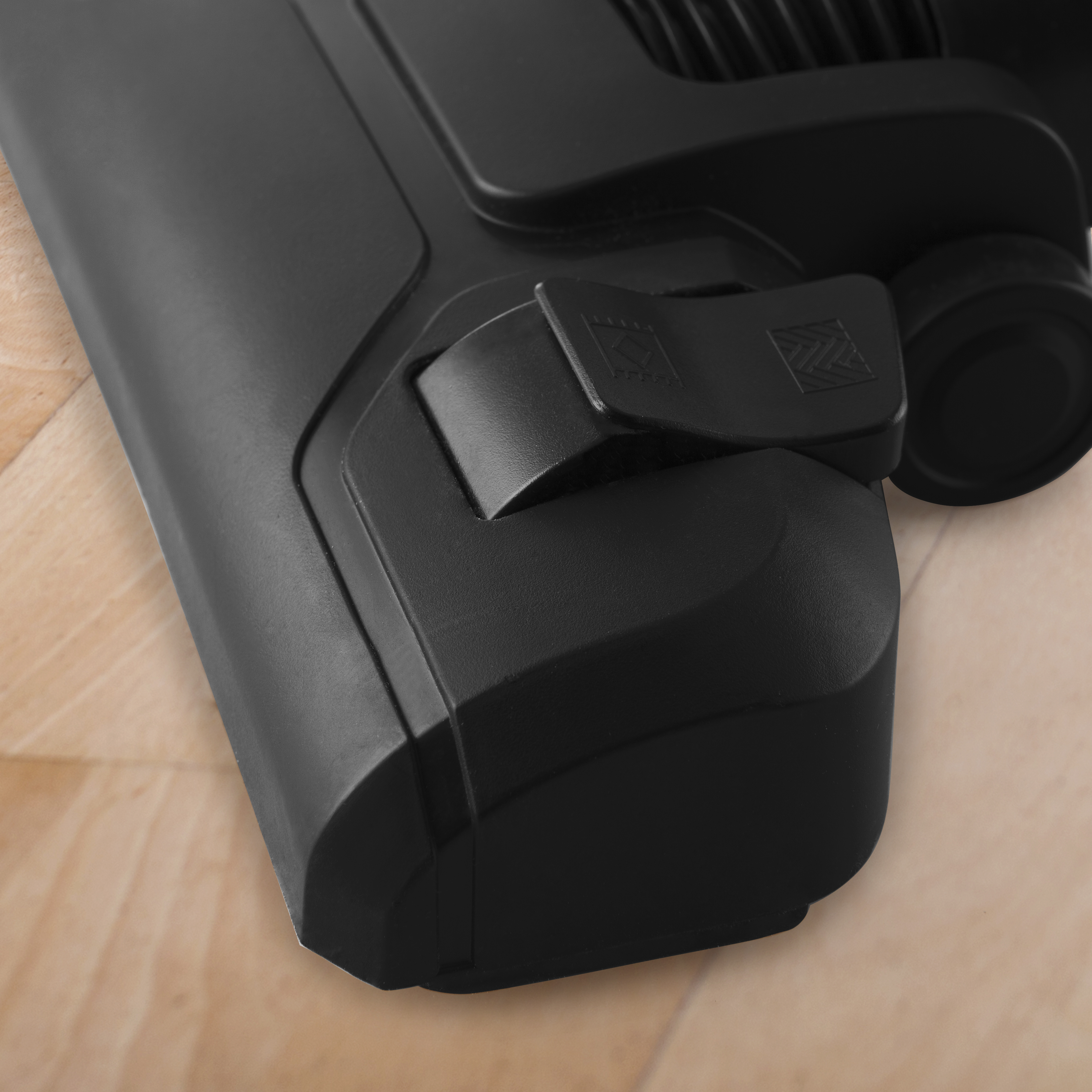 Czarny osprzęt do odkurzacza. Widok pod kątem. Pokazuje szczotkę i przycisk. Drewniana podłoga w tle.