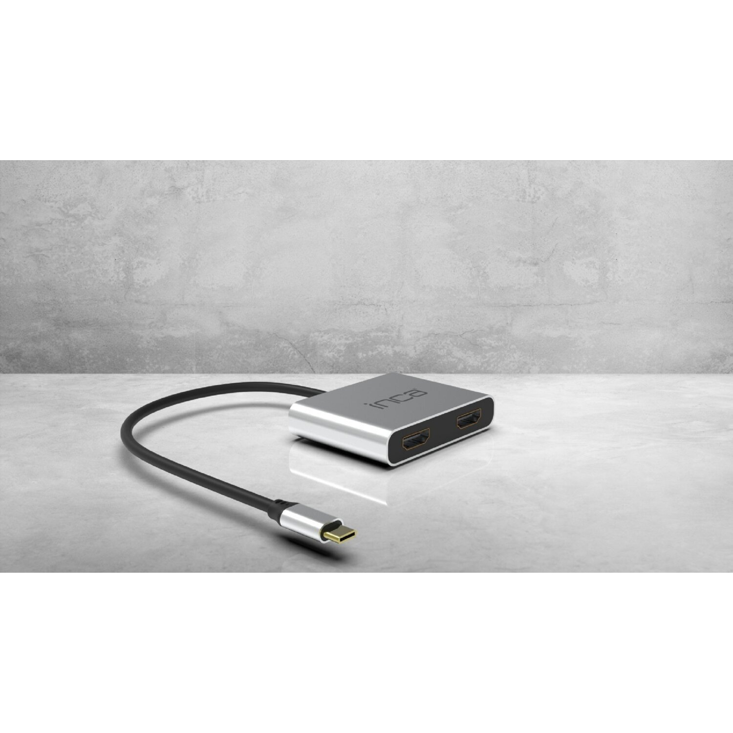 Adattatore HDMI argentato con cavo nero, su una superficie grigio chiaro.