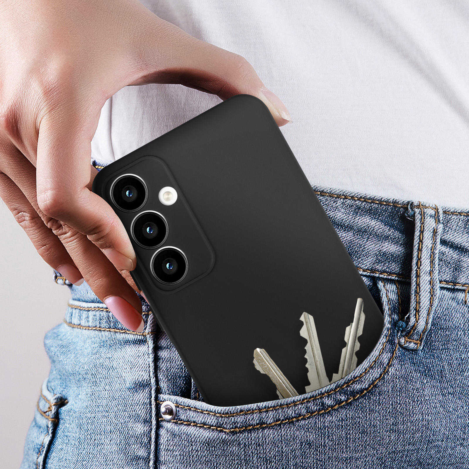 Una mano che mette un telefono nero in tasca con delle chiavi. Il telefono ha tre fotocamere.