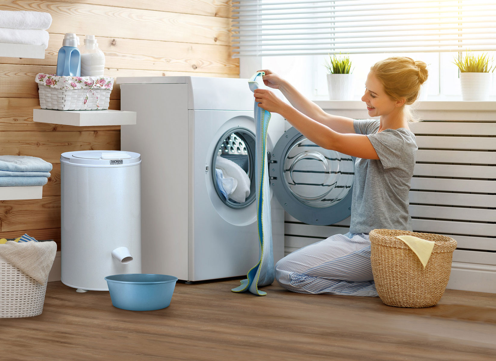 Woman putting a colorful towel into a washing machine. Laundry room setting with wooden wall.