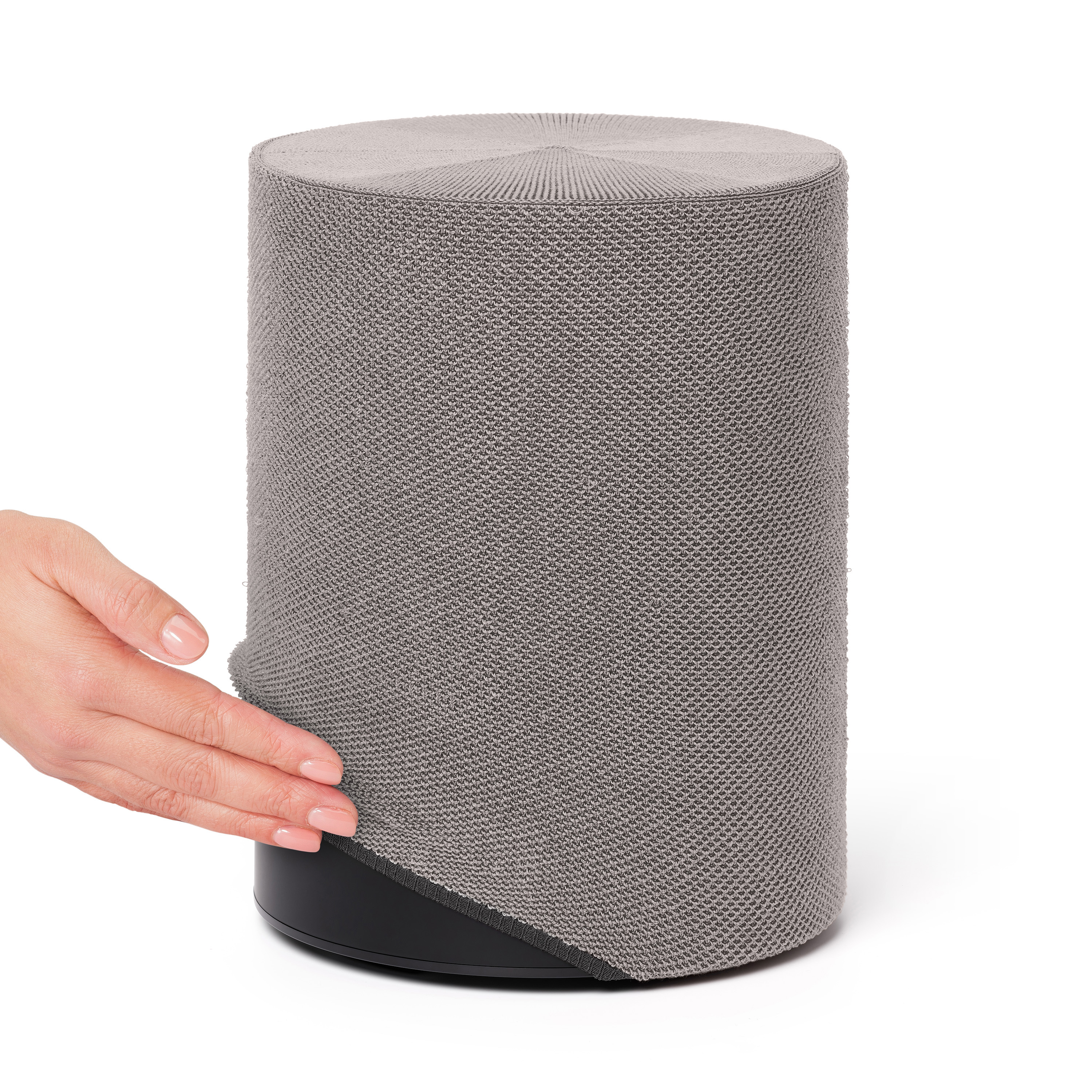 Un haut-parleur cylindrique gris avec une housse en tissu. Une main tire le tissu vers le bas.
