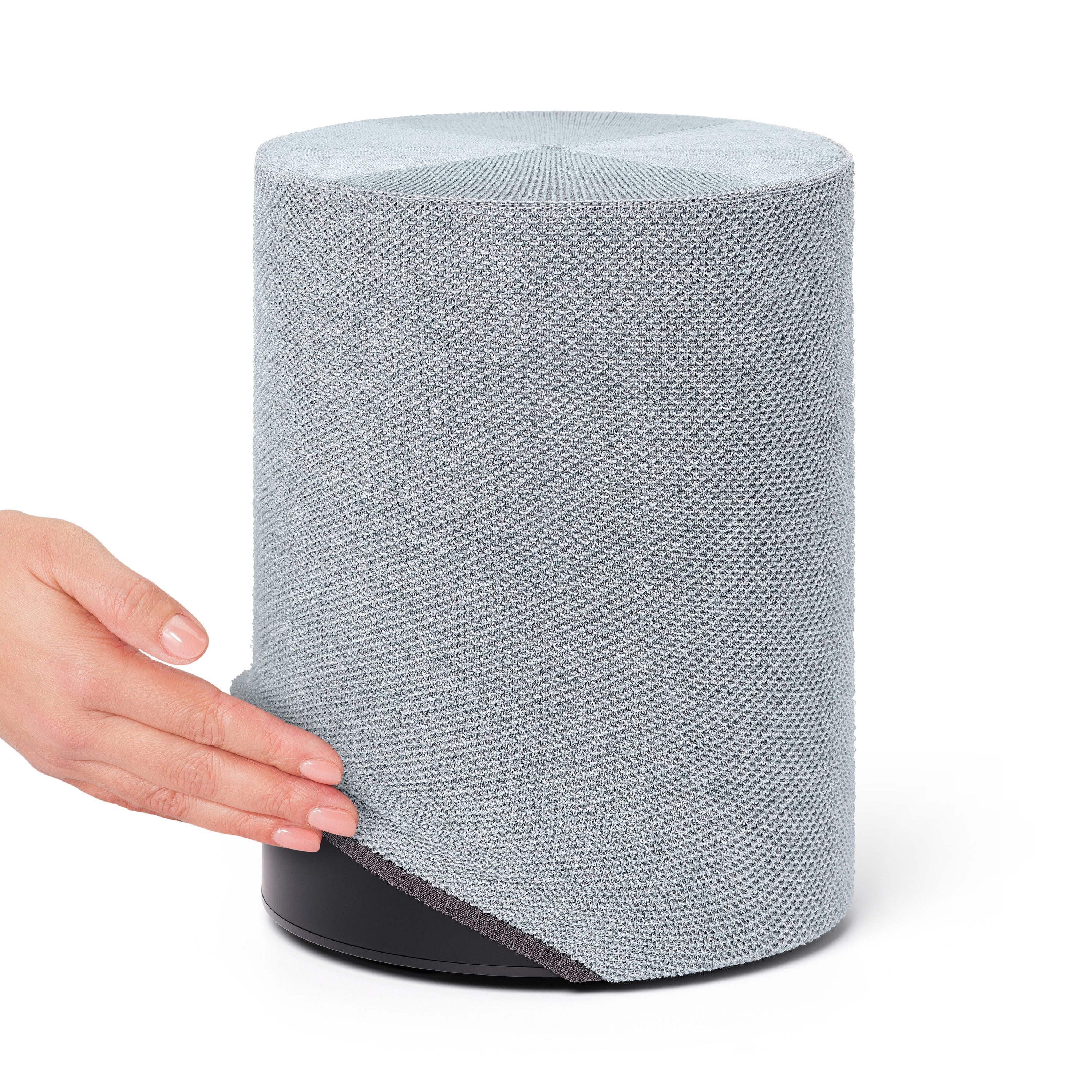 Haut-parleur gris clair avec une main qui le touche. Le haut-parleur est cylindrique sur une base noire.
