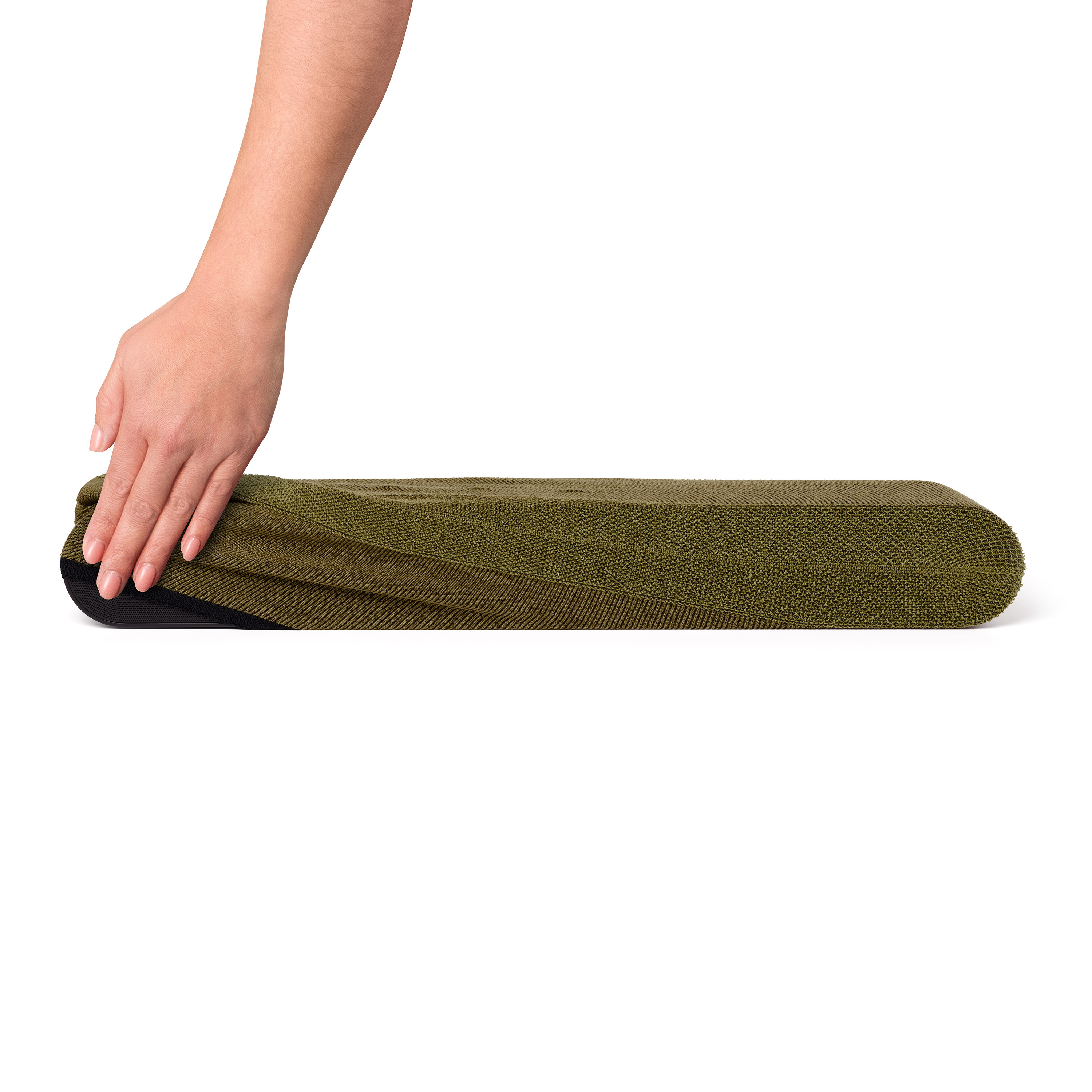 Une main plie un tapis rayé vert et noir. Le tapis est plié sur un fond blanc.