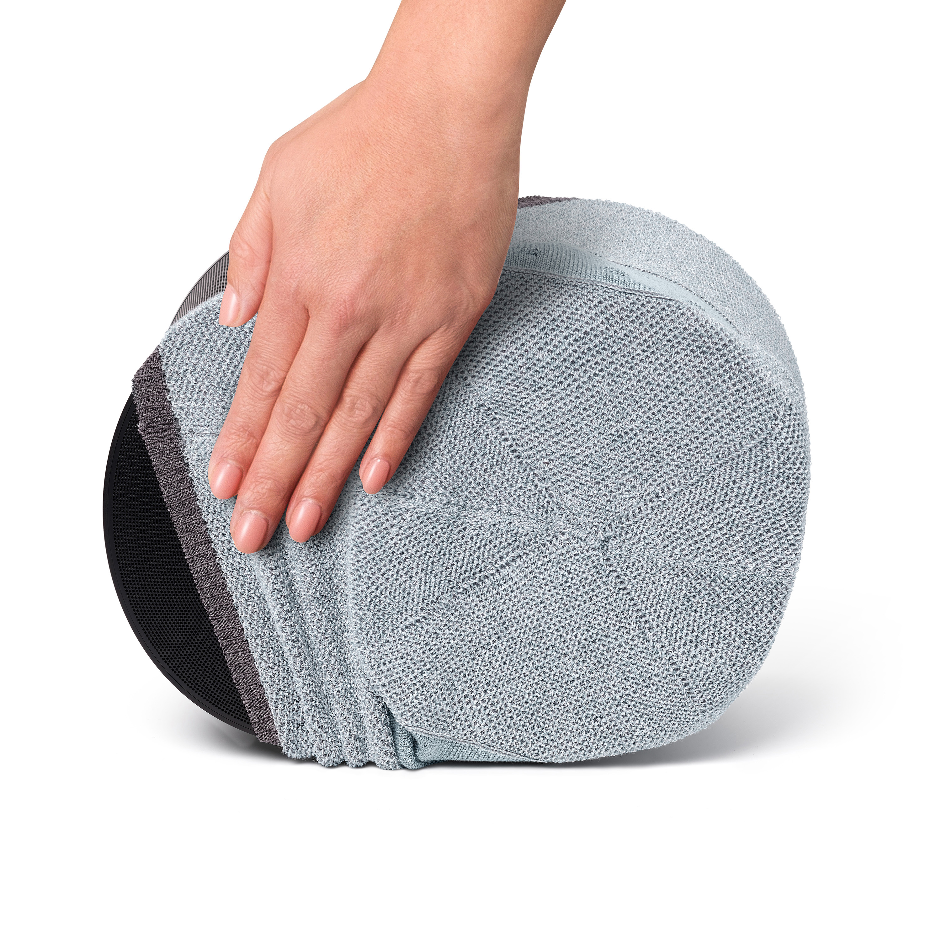 Hand die een grijs, afgerond kussen met een zwarte basis aanraakt op een witte achtergrond.
