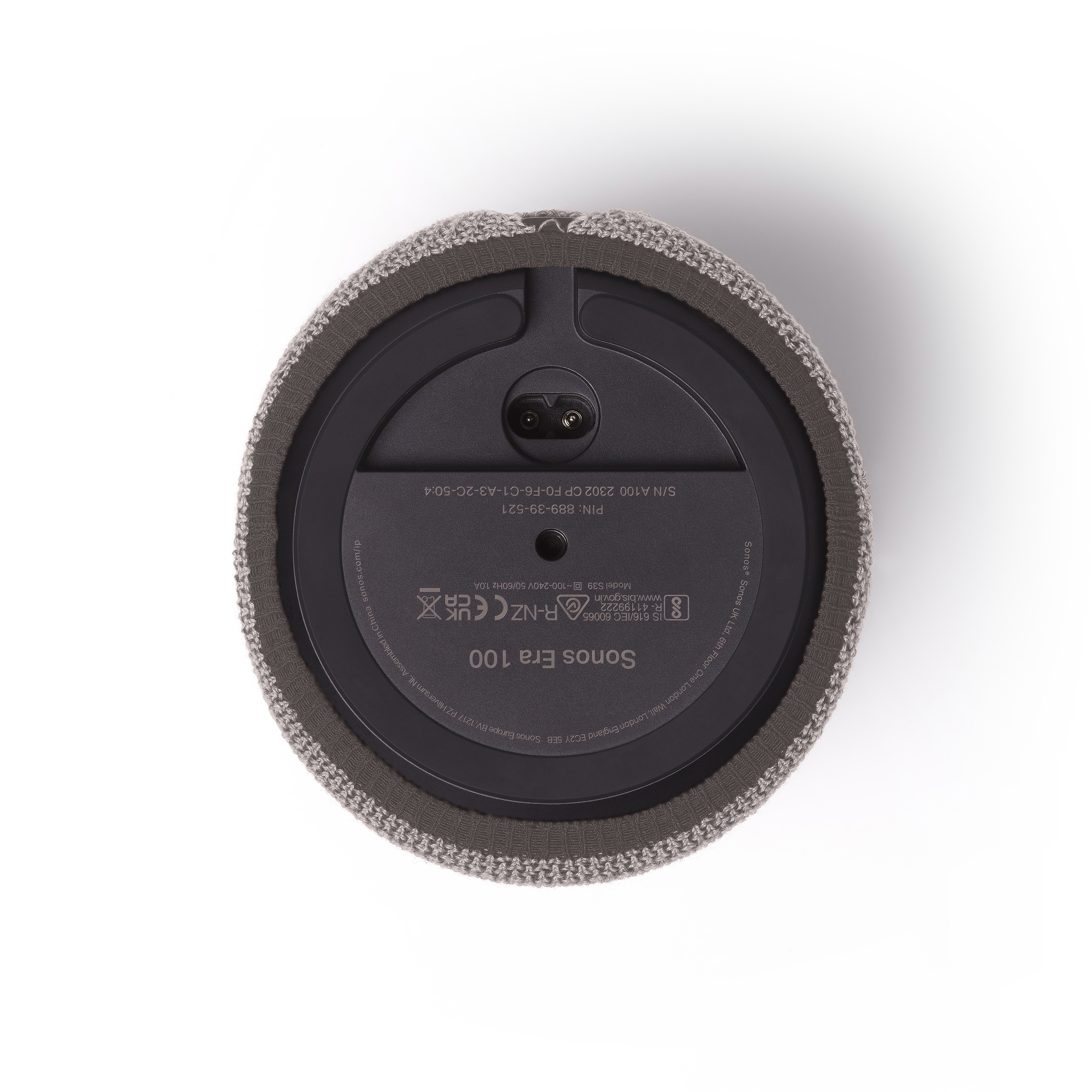 Onder aanzicht van een grijze Sonos Era 100 speaker, met labels en een voedingspoort, op een wit oppervlak.