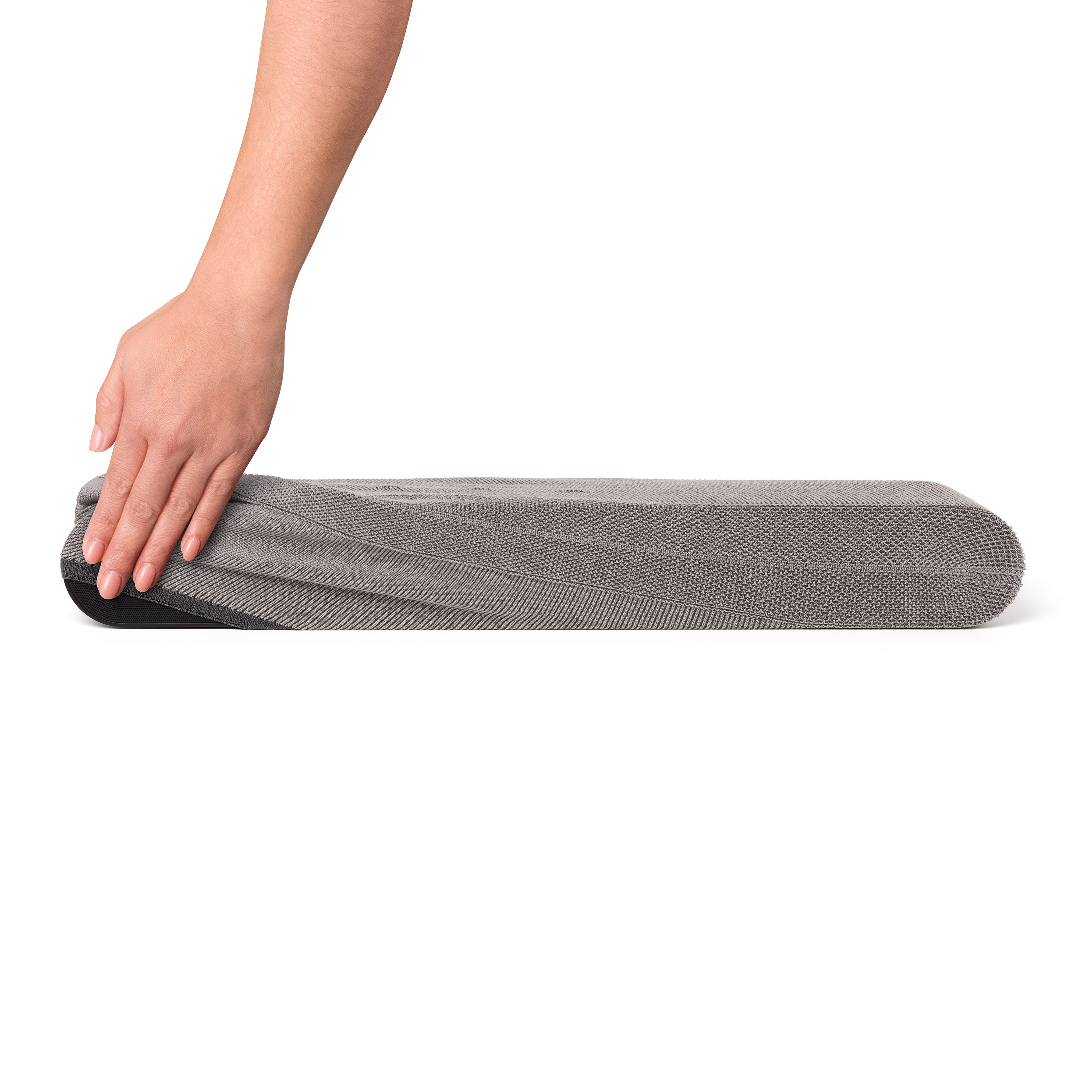 Une main enroule un tapis gris plié et strié sur fond blanc.
