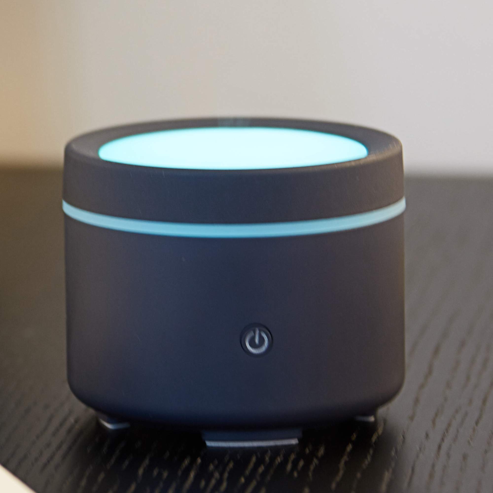 Black, cylindrical smart diffuser with a light blue glow. The power button is visible.