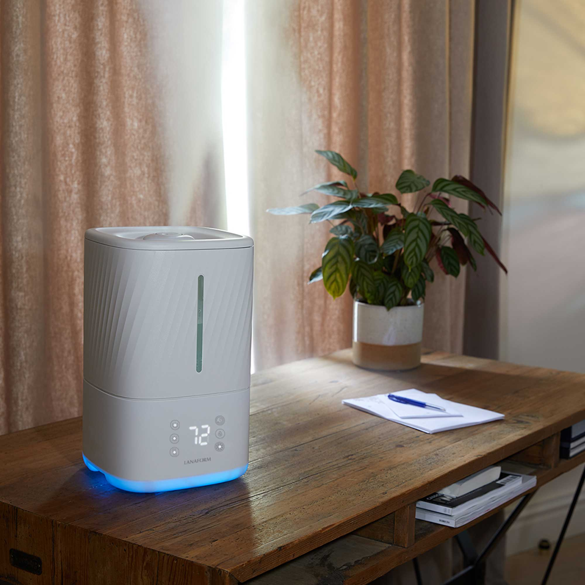 White humidifier with a display, a plant, and a notepad on a wooden desk.