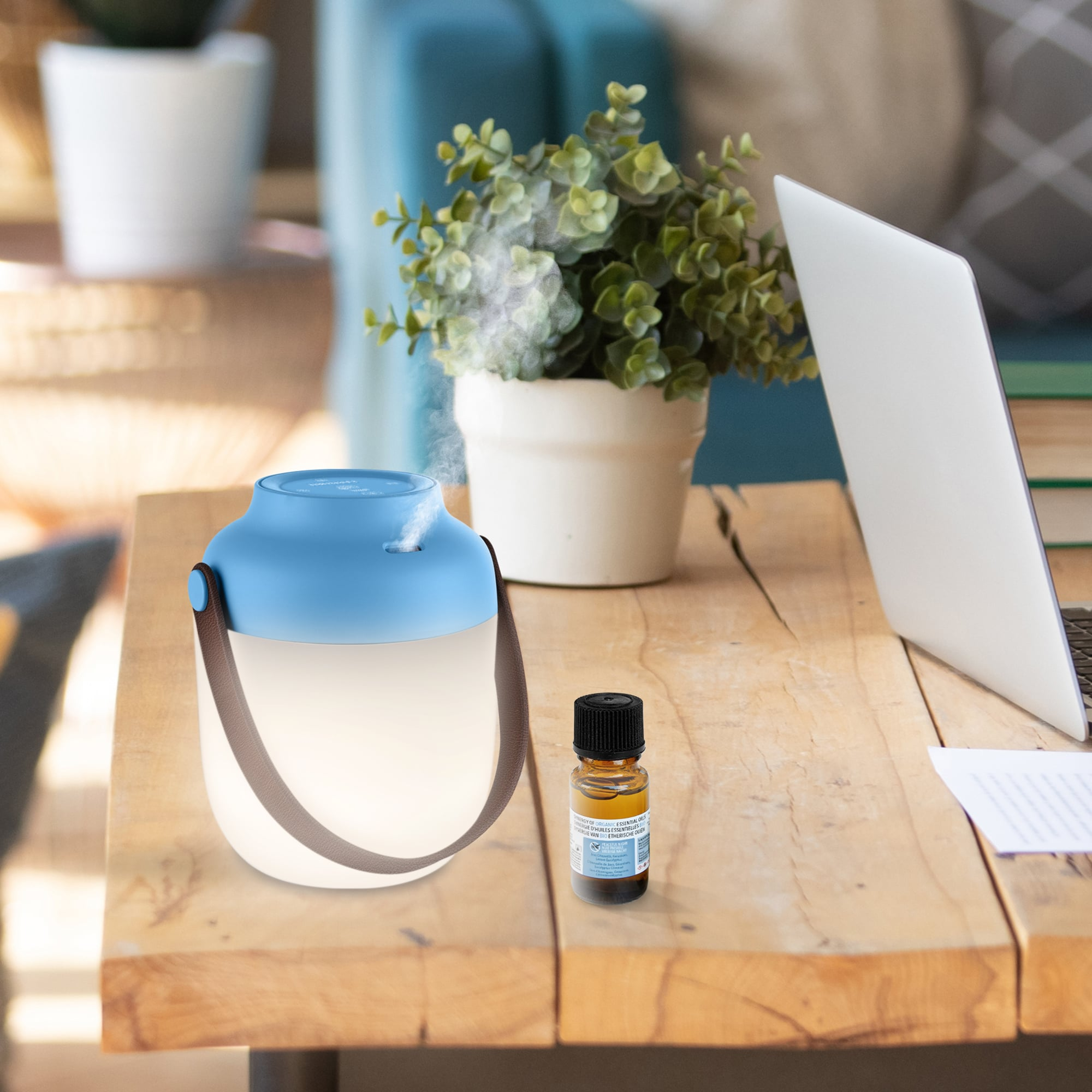 Aroma diffuser with a blue top and a small bottle of essential oil on a wood table.