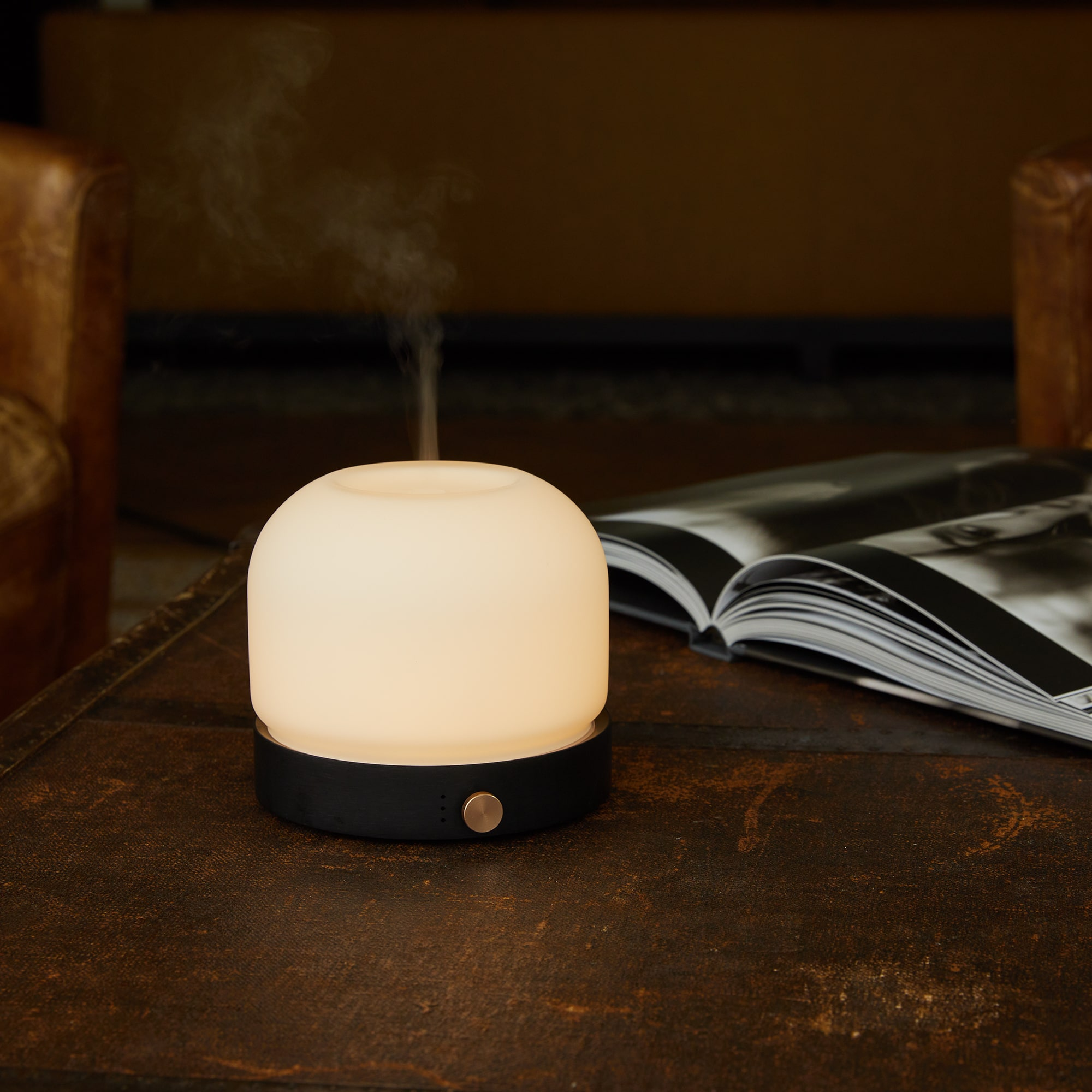 White and black aroma diffuser on a table. A magazine is open, and vapor is rising.