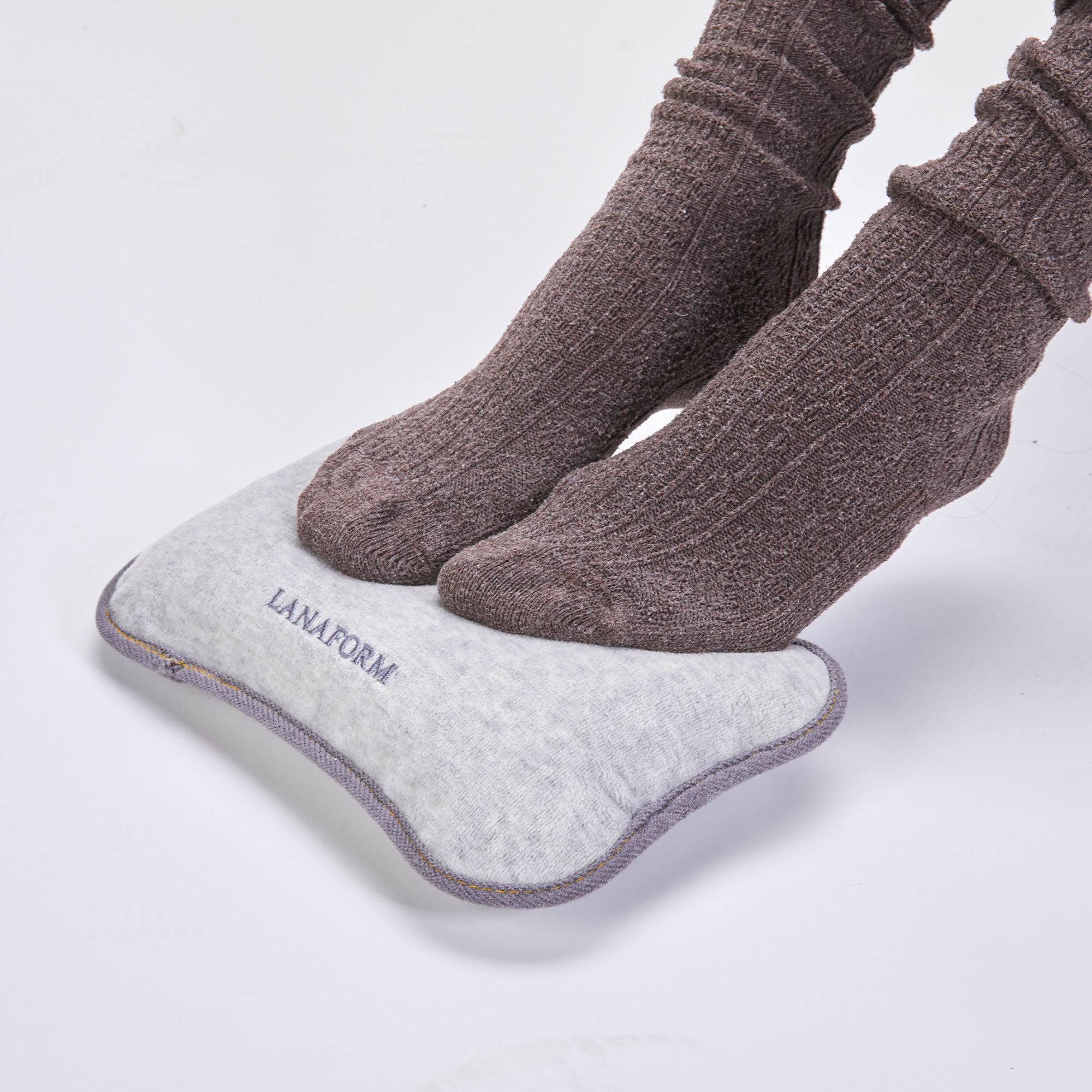 Füße in braunen Socken auf einem grauen LANAFORM Fußwärmer-Pad, weißer Hintergrund.