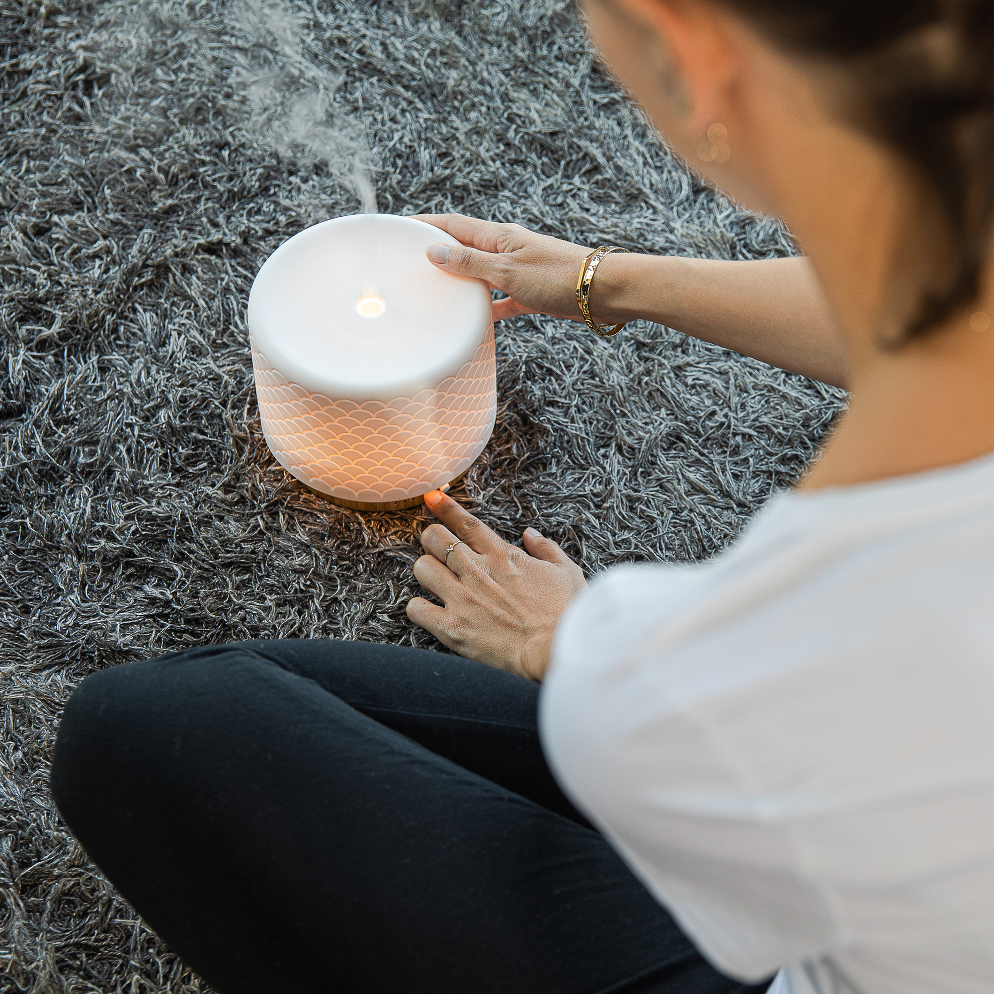 Eine Frau benutzt einen Aroma-Diffusor auf einem grauen Teppich. Der Diffusor hat ein Muster.