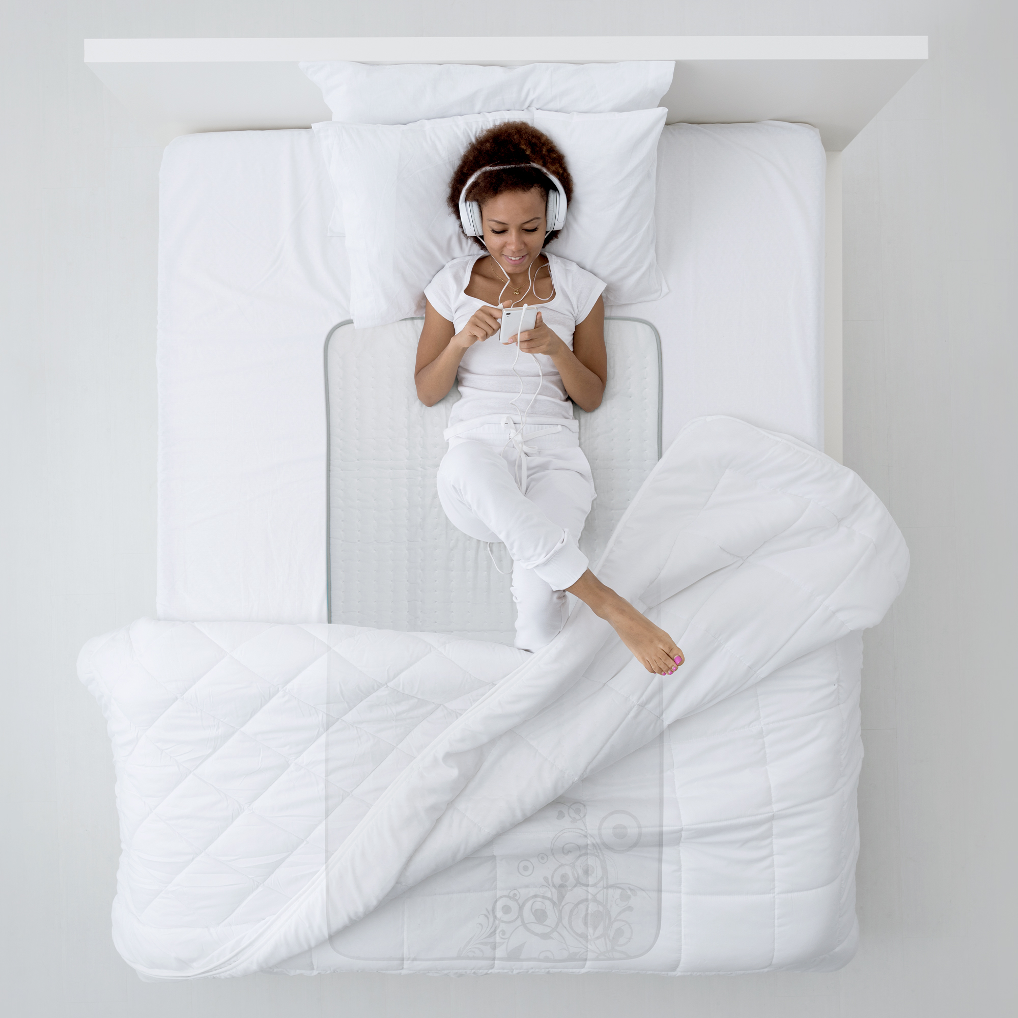 Eine Frau mit Kopfhörern liegt auf dem Bett und benutzt ihr Handy, mit einer Decke bedeckt.