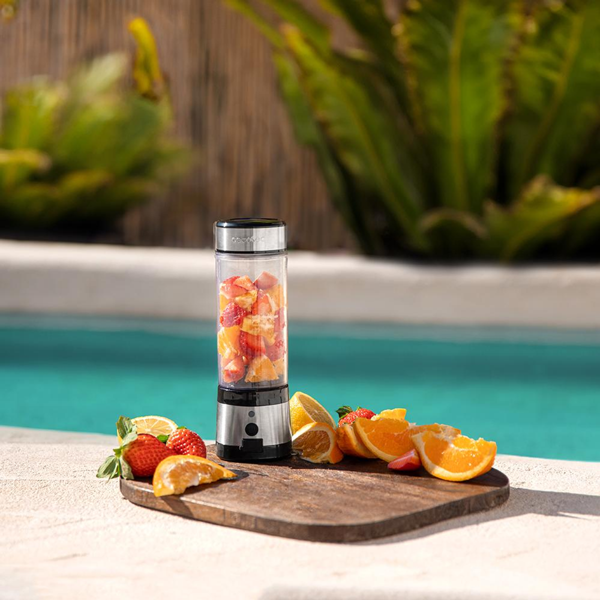 Frullatore con frutta all'interno su un tagliere di legno. Fragole, arance, limoni e acqua.