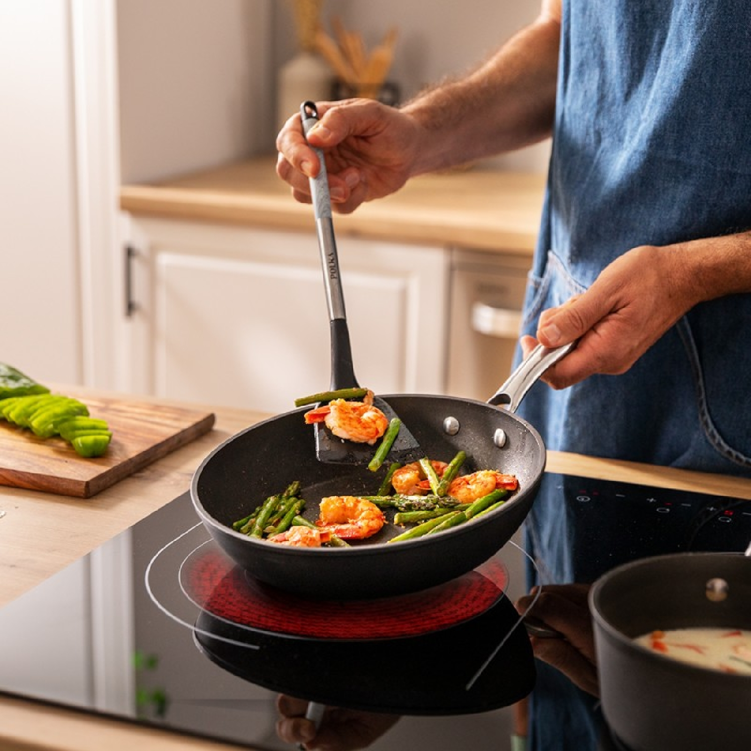 Persona che cucina gamberi e asparagi in padella su un fornello rosso.