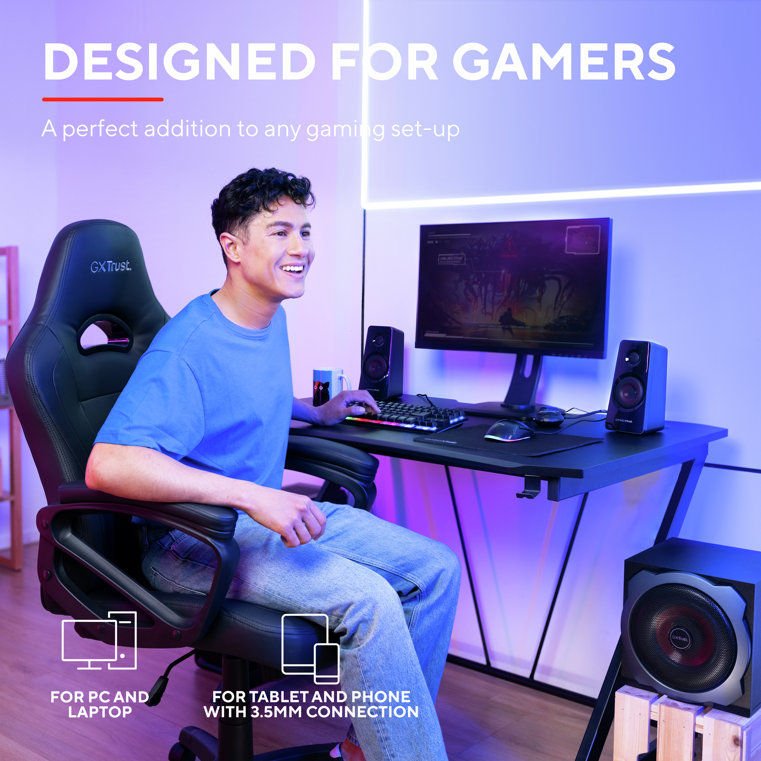 A man is gaming. He is in a gaming chair, with a monitor, speakers, and a subwoofer on a desk.