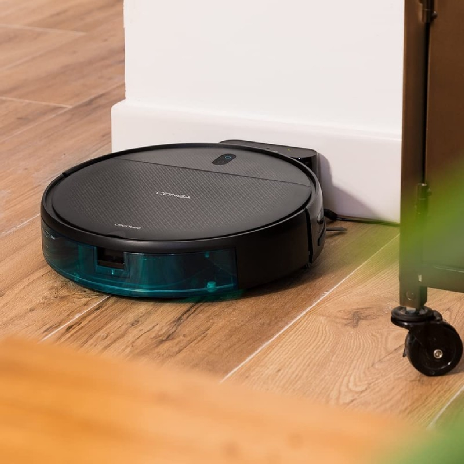 Robot aspirador en suelo de madera. Es negro y redondo.