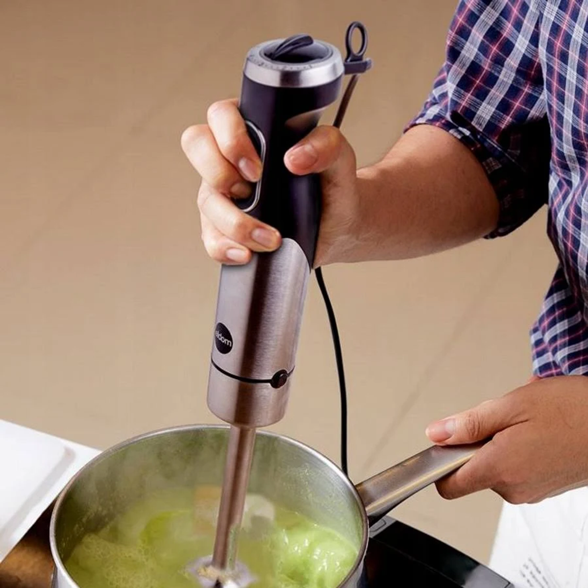 Persoon die soep in een pan mengt met een staafmixer, op een fornuis.