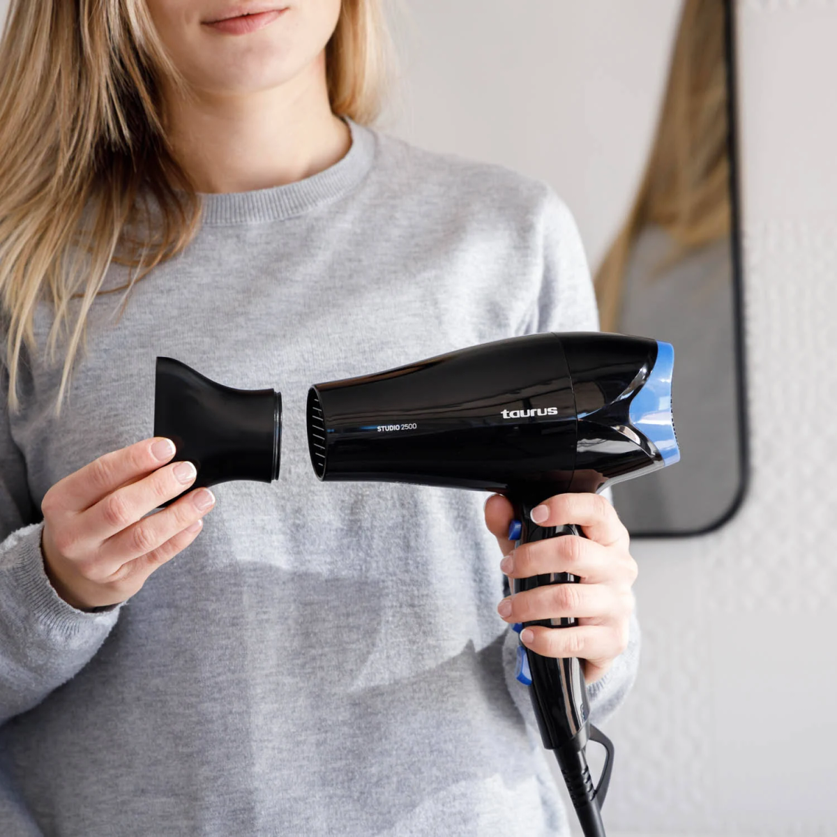 Una mujer sosteniendo un secador de pelo negro y azul. Está a punto de adjuntar un accesorio.