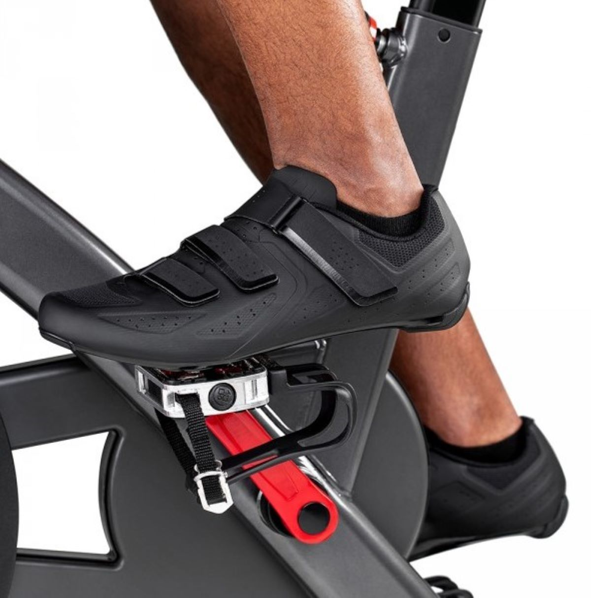 Stopa osoby w czarnym butie rowerowym jest wpięta w pedał roweru stacjonarnego.