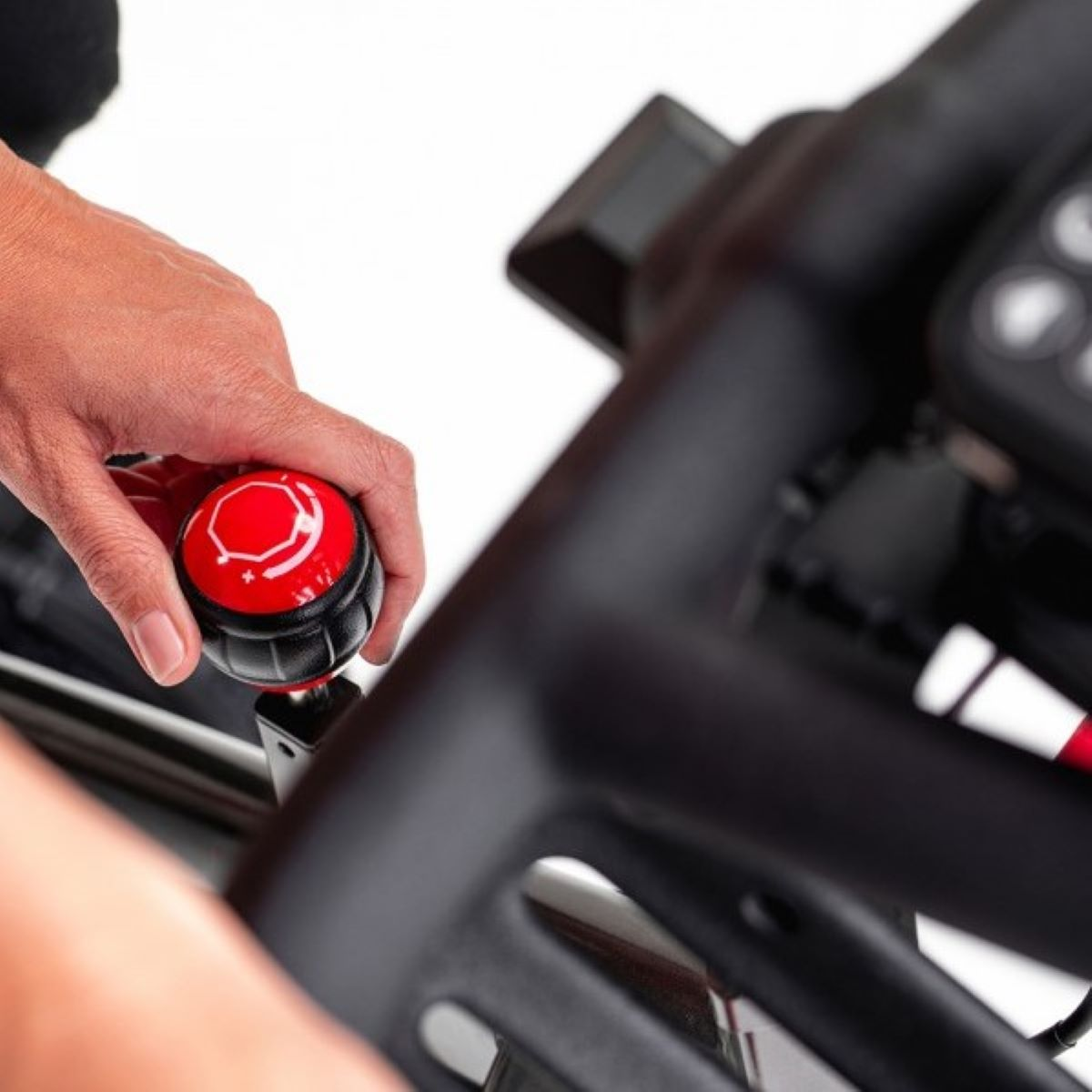 Ręka regulująca czerwono-czarne pokrętło na maszynie do ćwiczeń. Ujęcie z bliska.