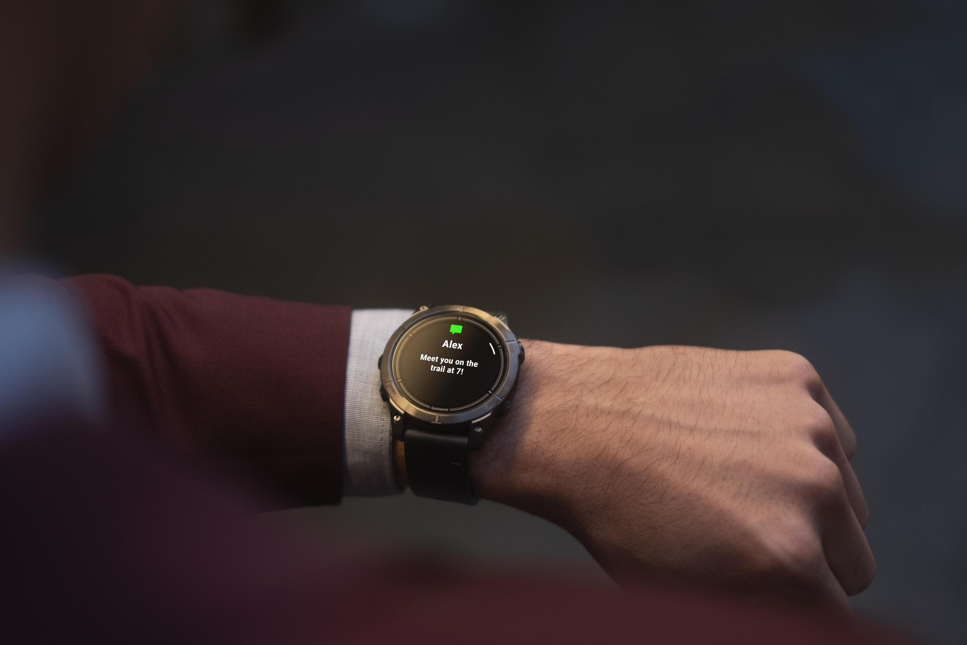 Smartwatch na nadgarstku wyświetlający wiadomość: 'spotkajmy się na szlaku o 7'.