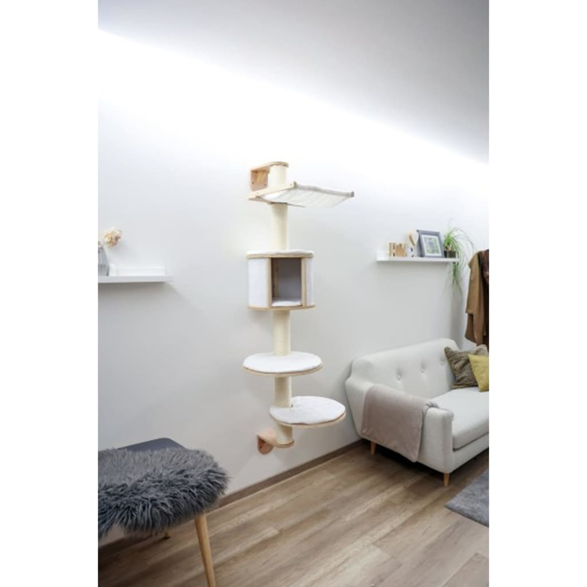 Katzenbaum mit mehreren Ebenen, Plattformen und einer Hängematte, vor einer weißen Wand neben einem Sofa.