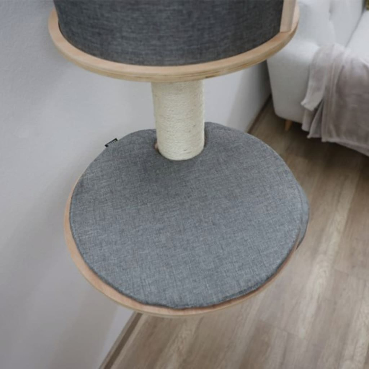An der Wand montiertes Katzengestell. Es hat ein kreisförmiges Bett mit grauem Stoff und eine Seilspalte.