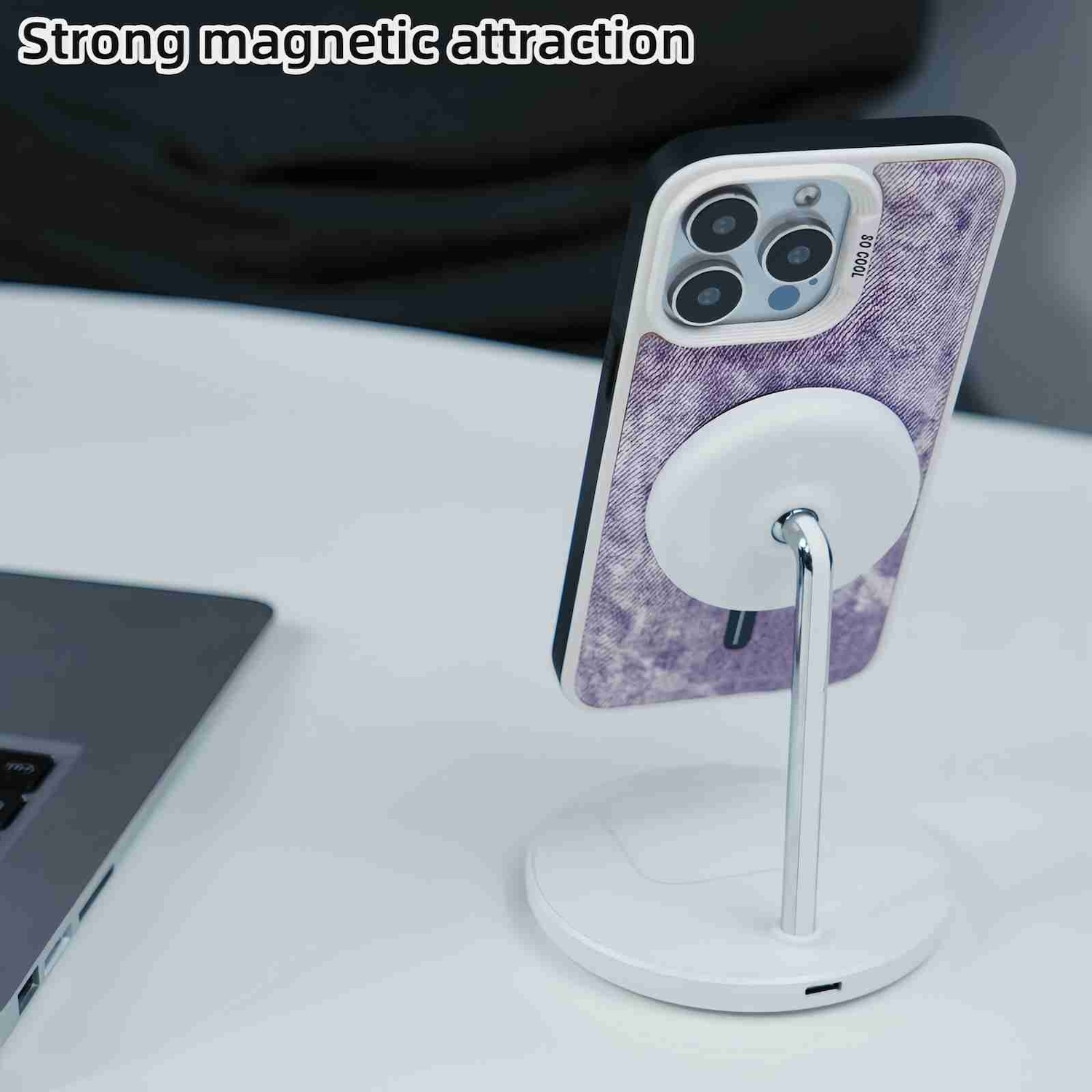 Telefon auf einem Ständer mit starker magnetischer Anziehungskraft. Laptop dahinter. Weißer Hintergrund.