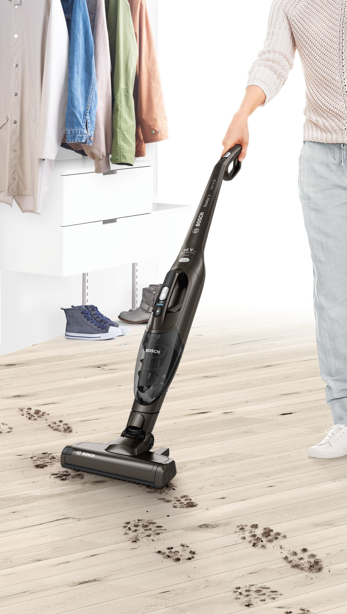 Persona che aspira un pavimento in legno con un aspirapolvere senza fili, mostrando impronte.