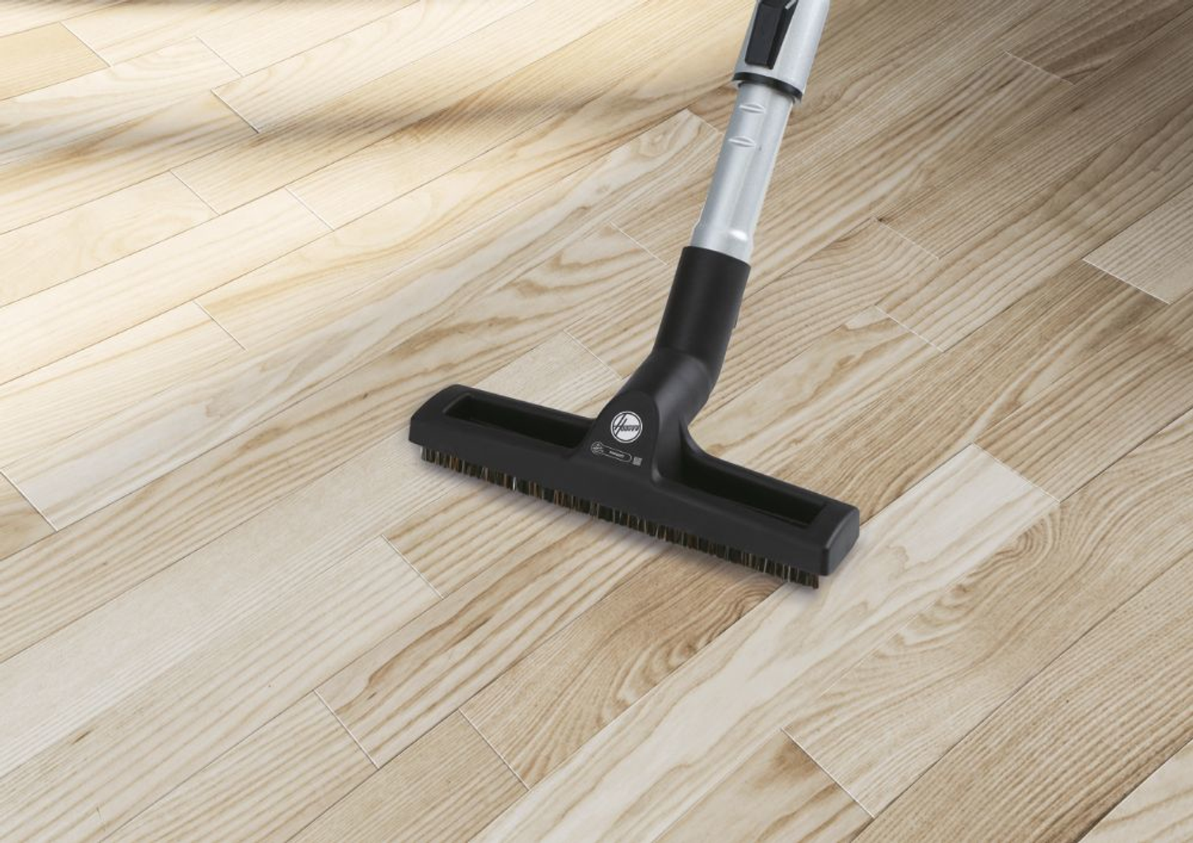 Głowica odkurzacza Hoover na drewnianej podłodze, pod kątem. Pokazuje włosie i czarny, zakrzywiony design.