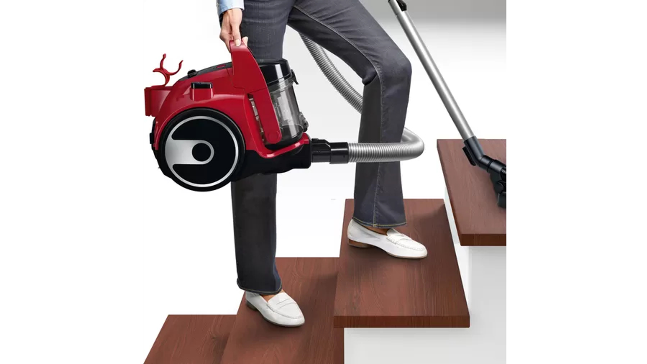 Osoba w dżinsach i białych butach odkurza schody czerwoną odkurzaczem.
